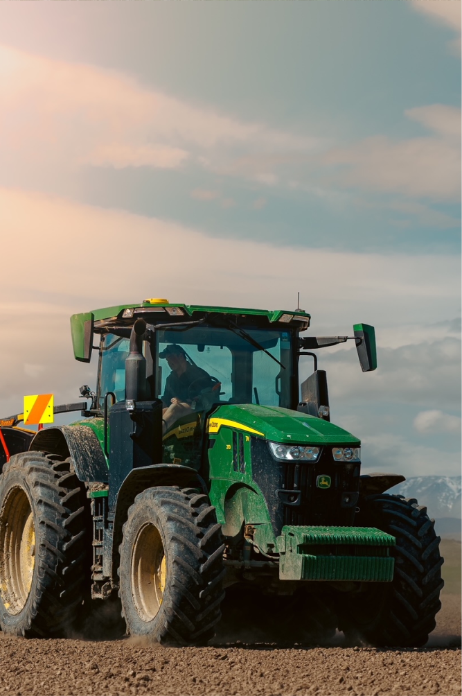 Green tractor plowing dirt on a farm with a cloudy sky background.