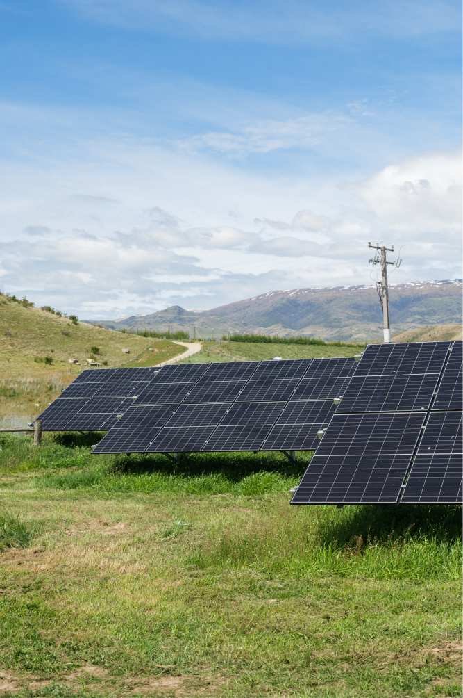 Solar panels installed on a grassy field with mountains and a partly cloudy sky in the background.