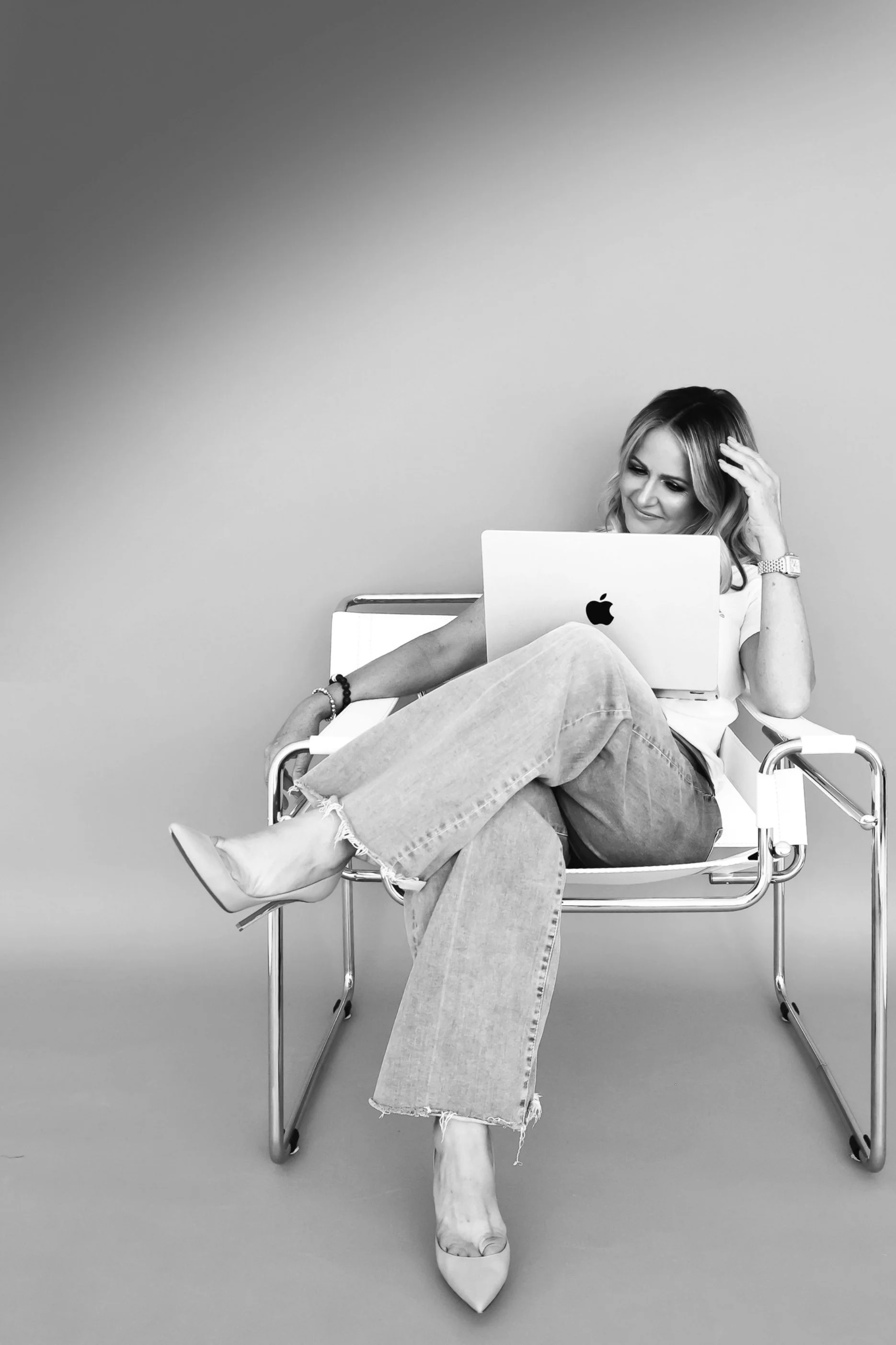 Black and white photo of Lisa Cole sitting on white chair with laptop.