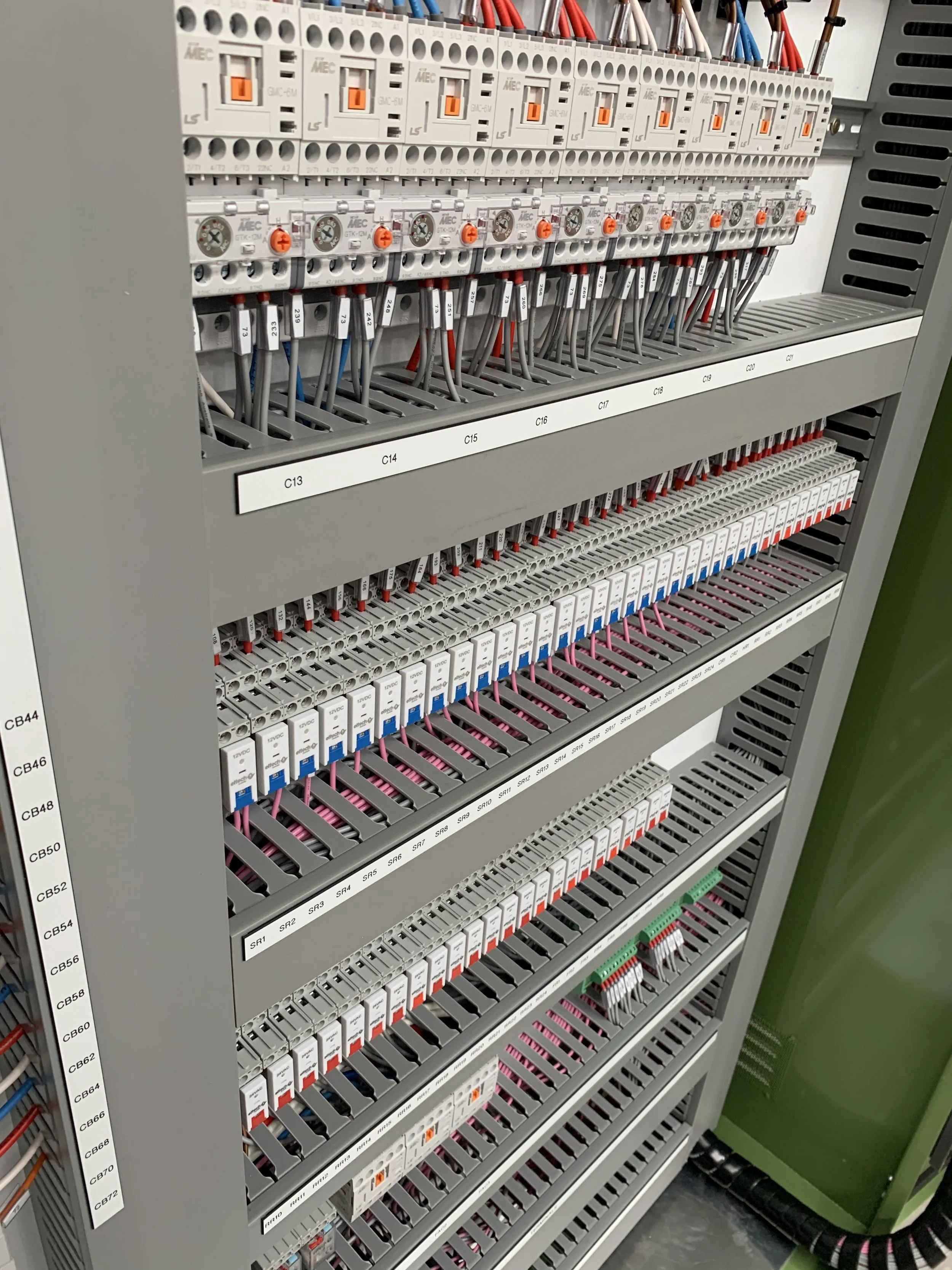 A control panel with multiple circuit breakers, electrical wires, and colored wiring organized in rows inside a gray metal enclosure.