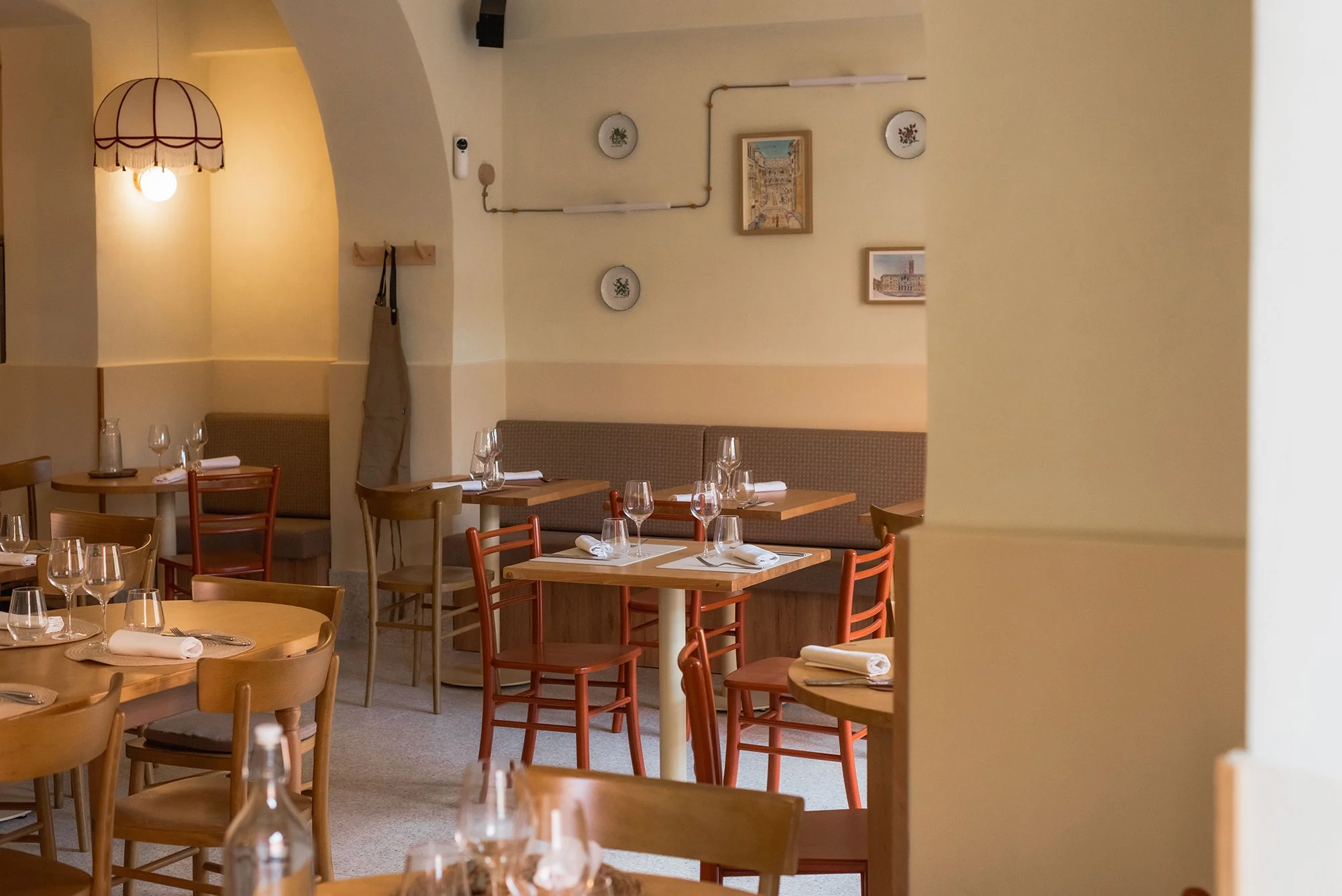 Interno di ristorante con tavoli apparecchiati, bicchieri e posate, decorazioni alle pareti e un lampadario sopra.