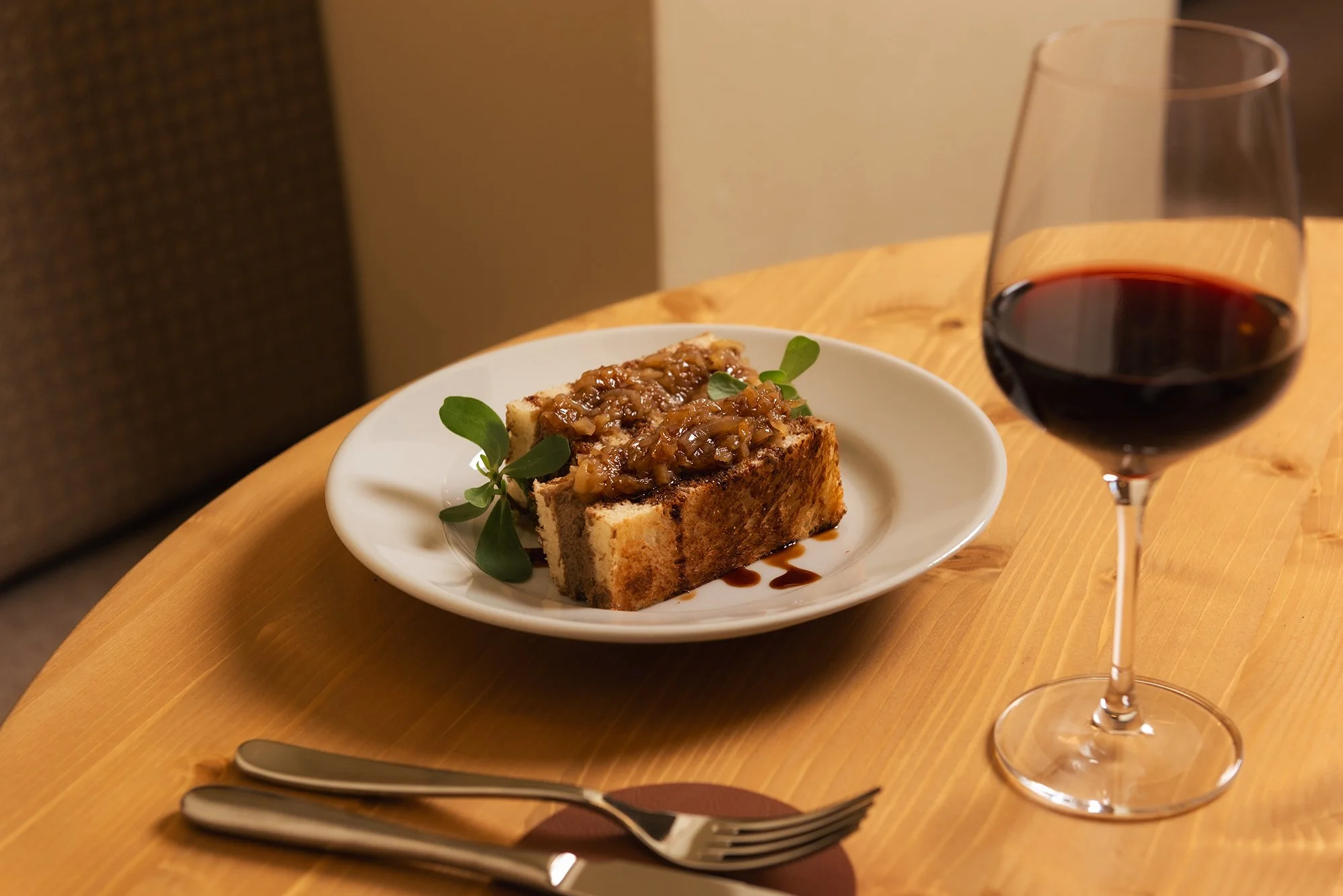 Secondo piatto, bicchiere di vino rosso, posate su tavolo di legno.