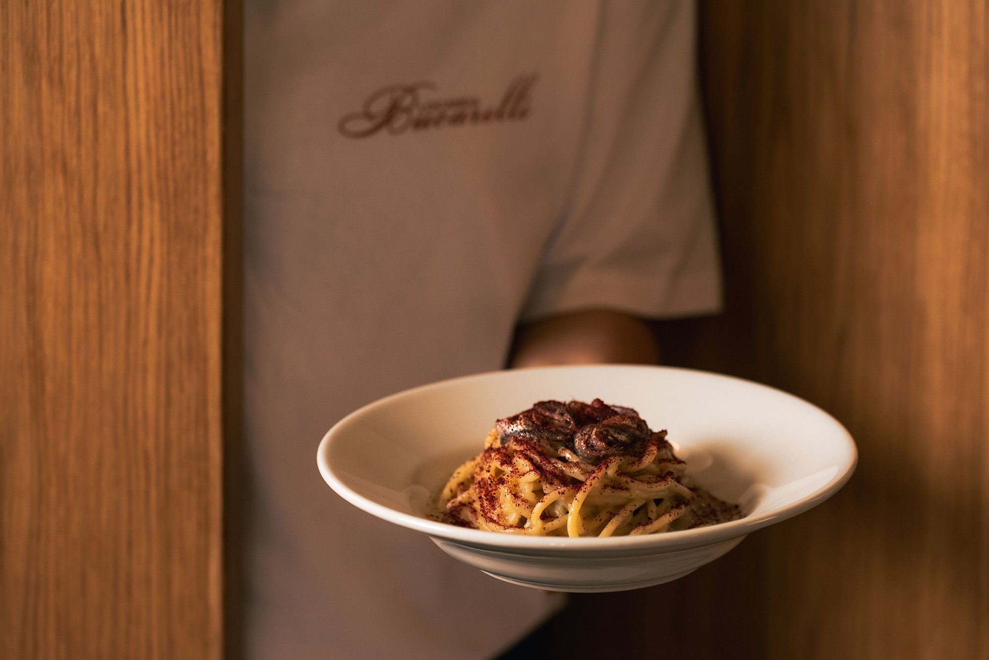 Piatti di pasta con condimento cremoso e guarniti con spezie, serviti in una ciotola bianca su tavolo di legno.
