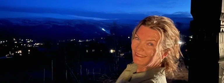 Portrett av kunstner Pia C. Bye som smiler, ute i blått kveldslys