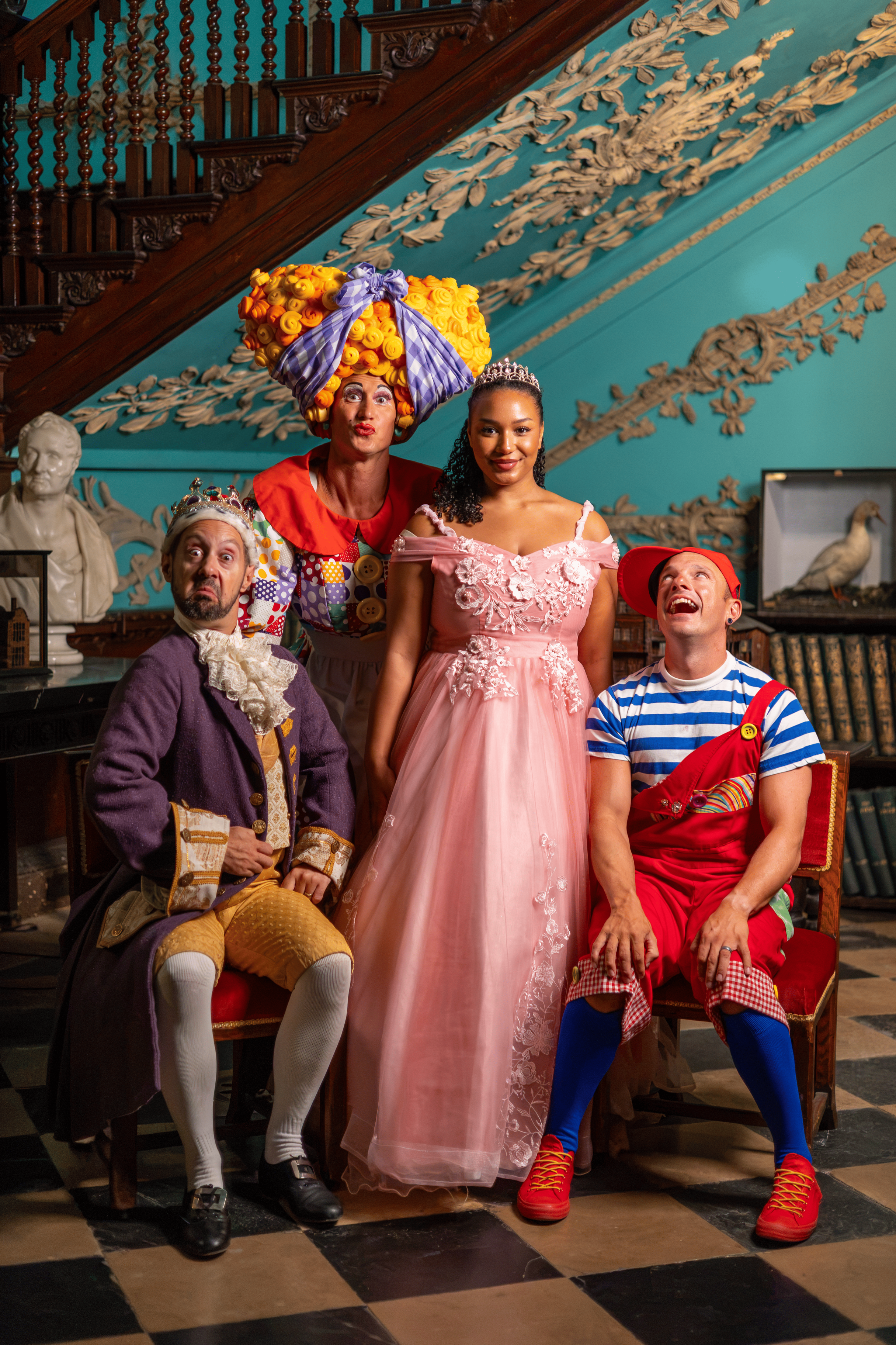 Four people dressed in colorful costumes posing in an ornate room with woodwork, a bust, and a taxidermied bird in the background.