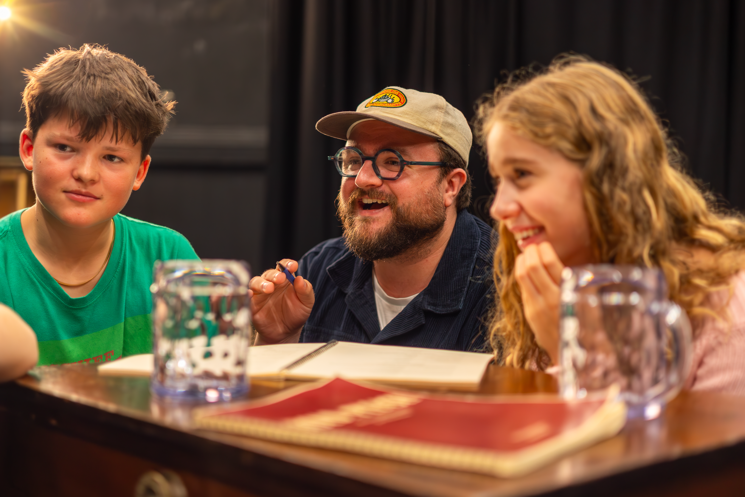 A group of three people sitting at a table, smiling. There is a young boy in a green shirt on the left, a man with a beard and glasses in the middle, and a woman with curly blond hair on the right. Photo by Lillie Sherry, Edinburgh.