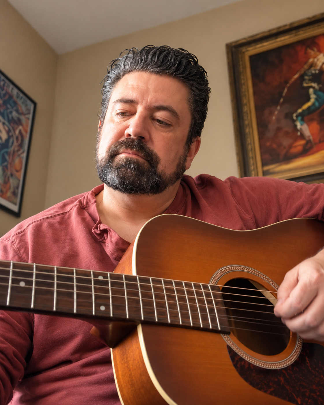 Bearded man in a red shirt playing an acoustic guitar indoors