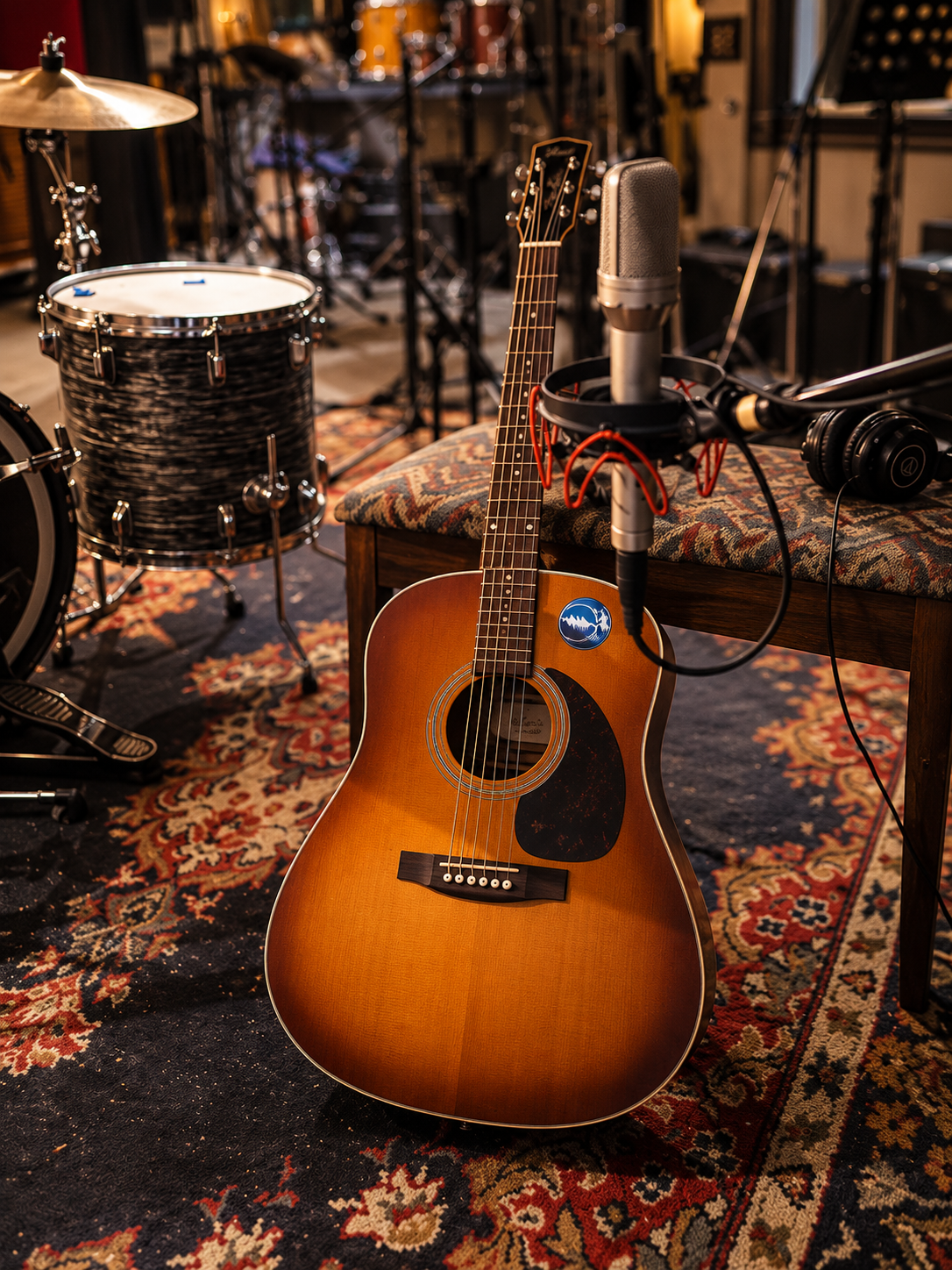Acoustic guitar and studio microphone in a recording studio with drums and headphones