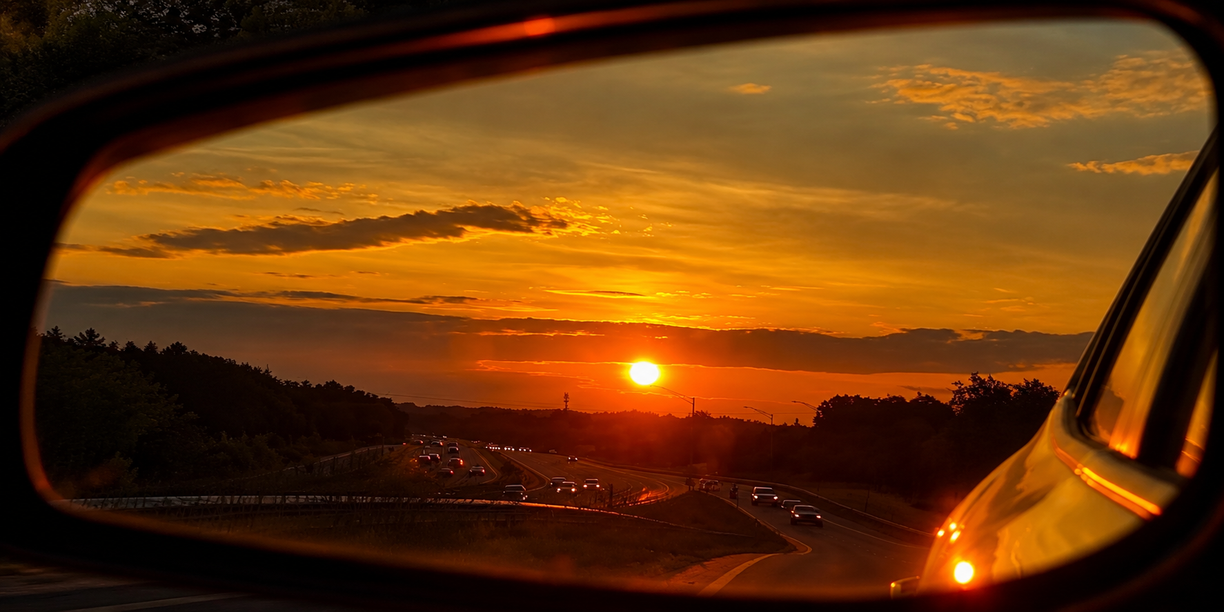 Golden sunset over a busy highway viewed through a car side mirror