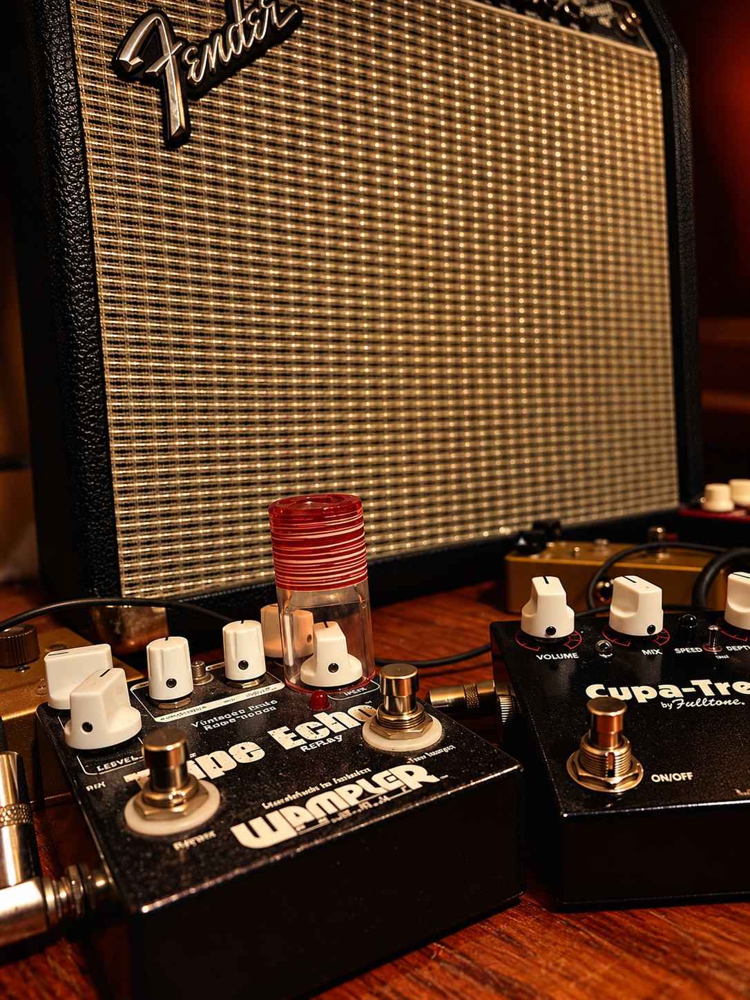 Close-up of guitar pedals, including a Fender amplifier, overdrive and tremolo effects pedals, on a wooden table.