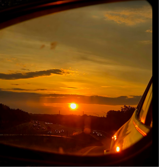 Orange sunset over a highway with traffic, viewed through a vehicle window