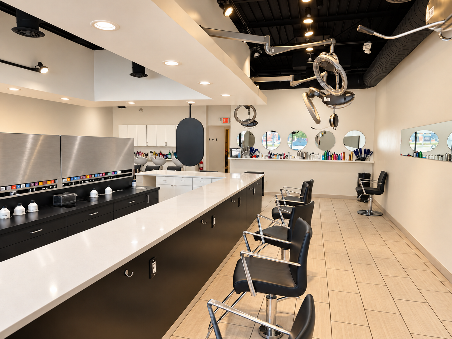 Empty modern hair salon with black and white color scheme, hair styling chairs, mirrors, and hair dye bottles on the counters.