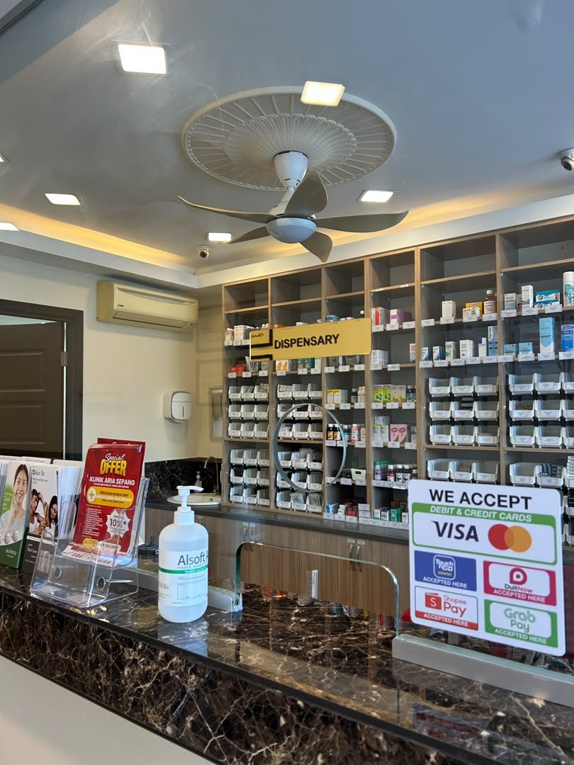 Inside a pharmacy with shelves of medication, a counter with hand sanitizer, and signs indicating accepted payment methods.