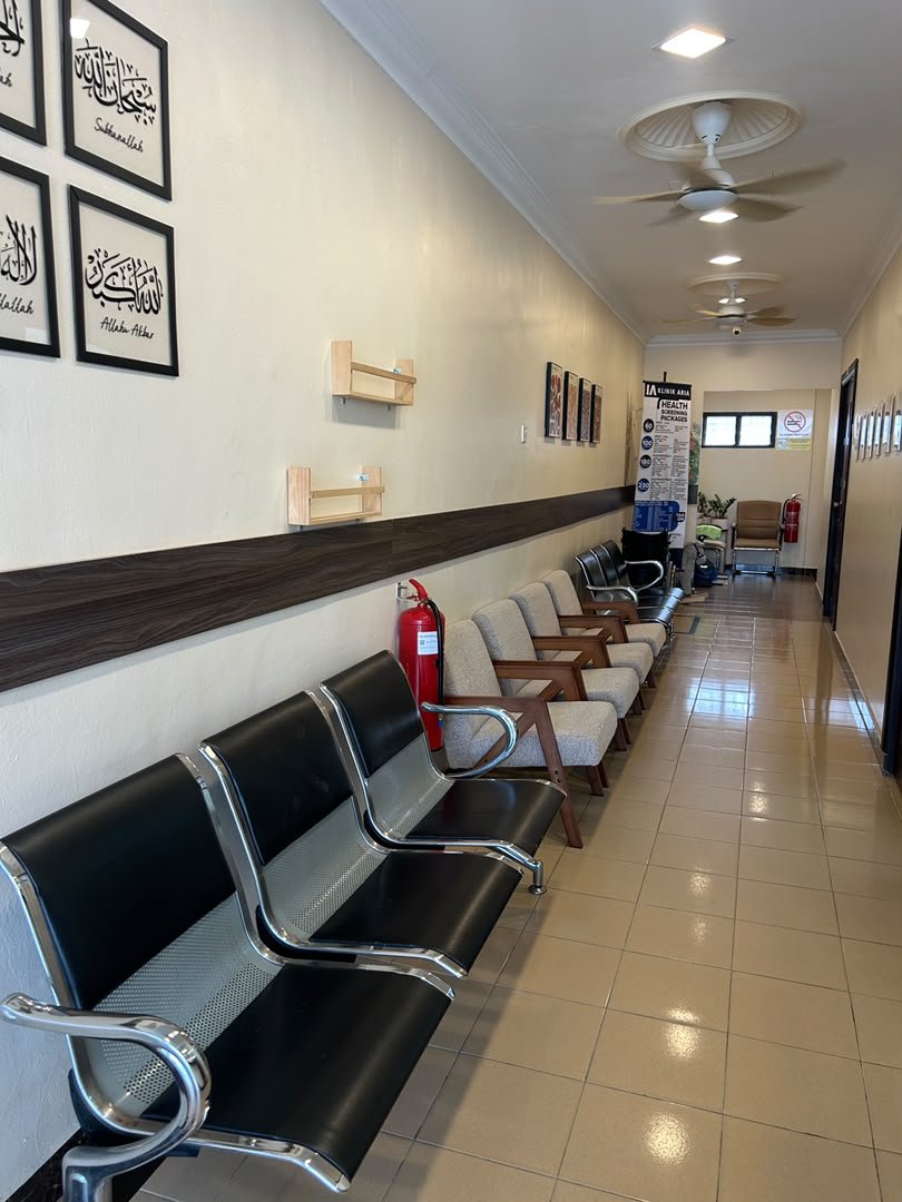 Empty waiting room with rows of black and beige chairs, a fire extinguisher, decorative framed art on the wall, and ceiling fans, in a well-lit space with a tiled floor.