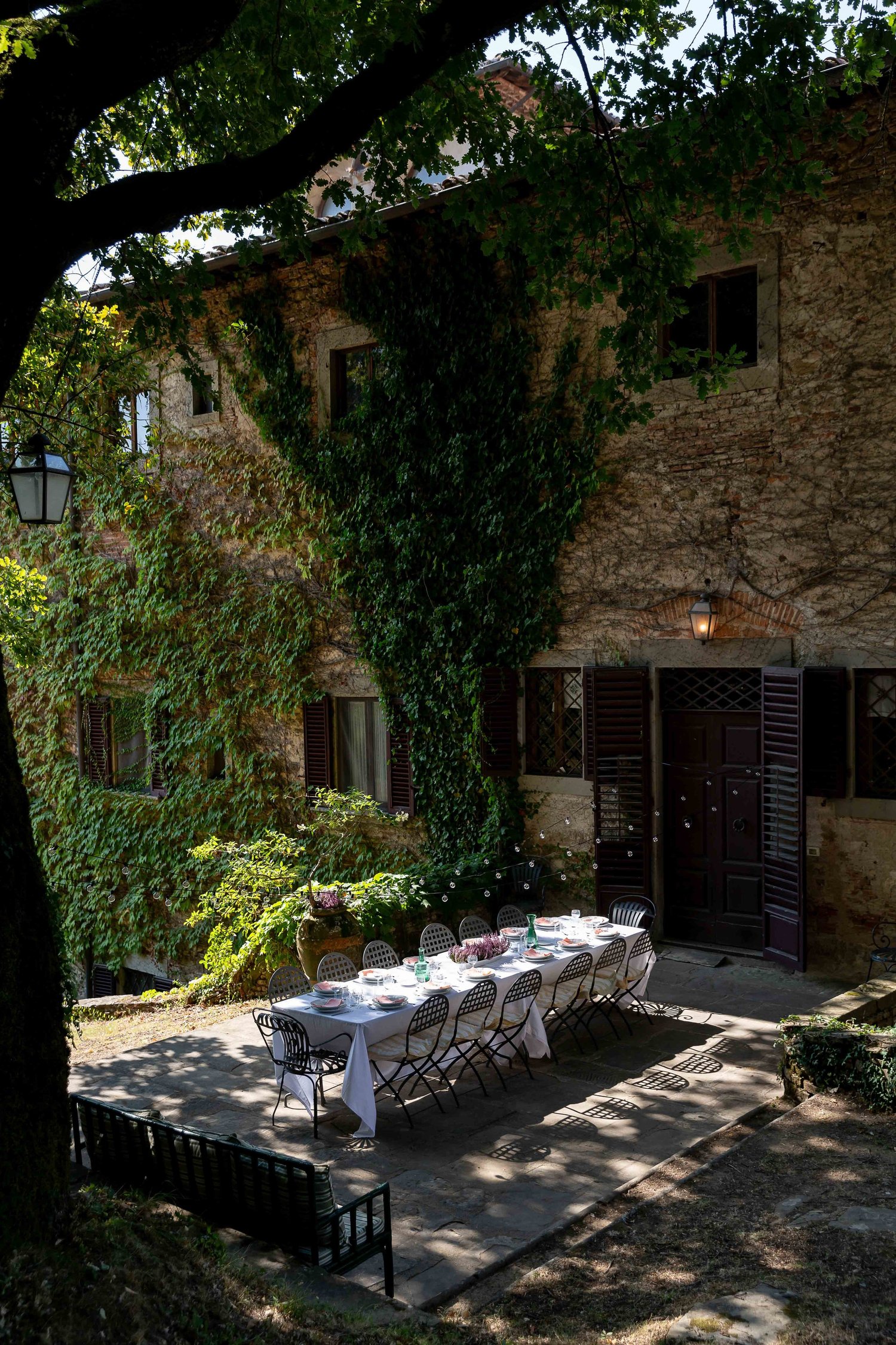 A long dining table beneath a tree beside the ivy-covered stone facade of Castello di Galbino.