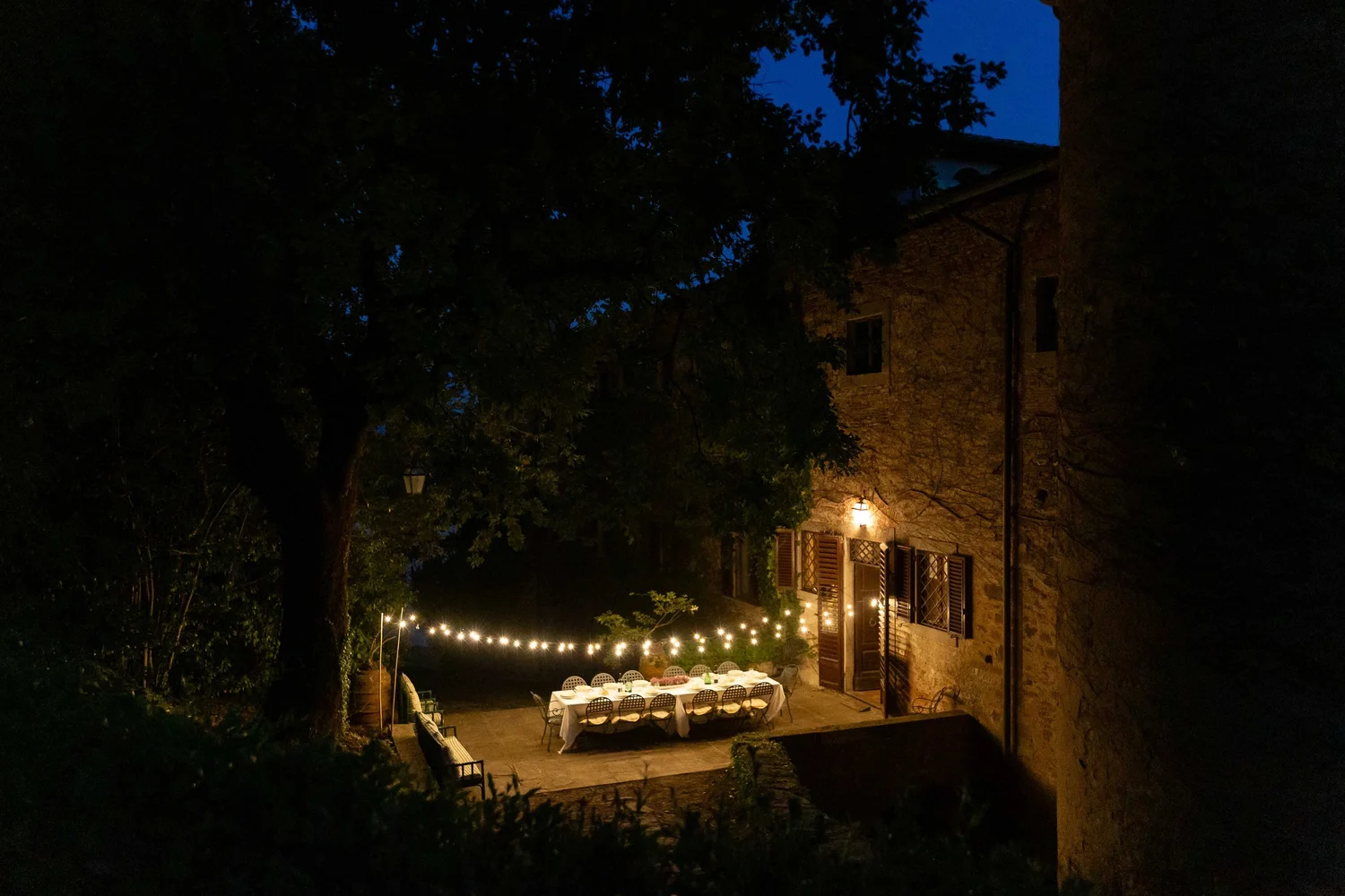A long dining table beneath string lights on the castle patio at night.