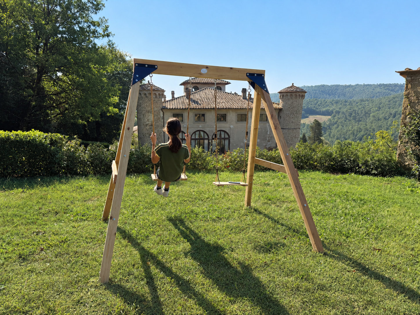 A child on a wooden swing in the garden, with Castello di Galbino and the Tuscan hills beyond.