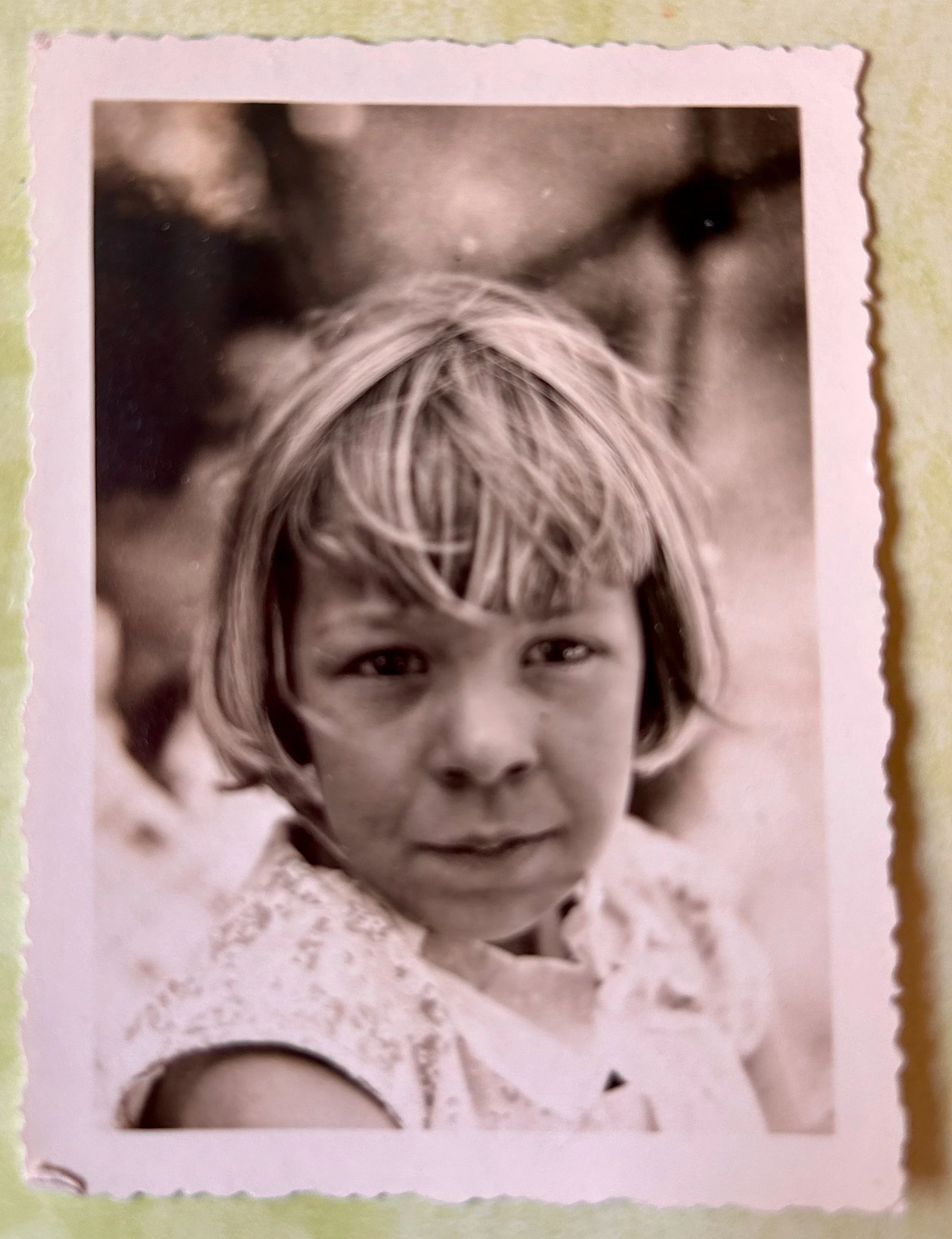 Black-and-white portrait of a smiling young girl with bangs, wearing a lace-trimmed top.