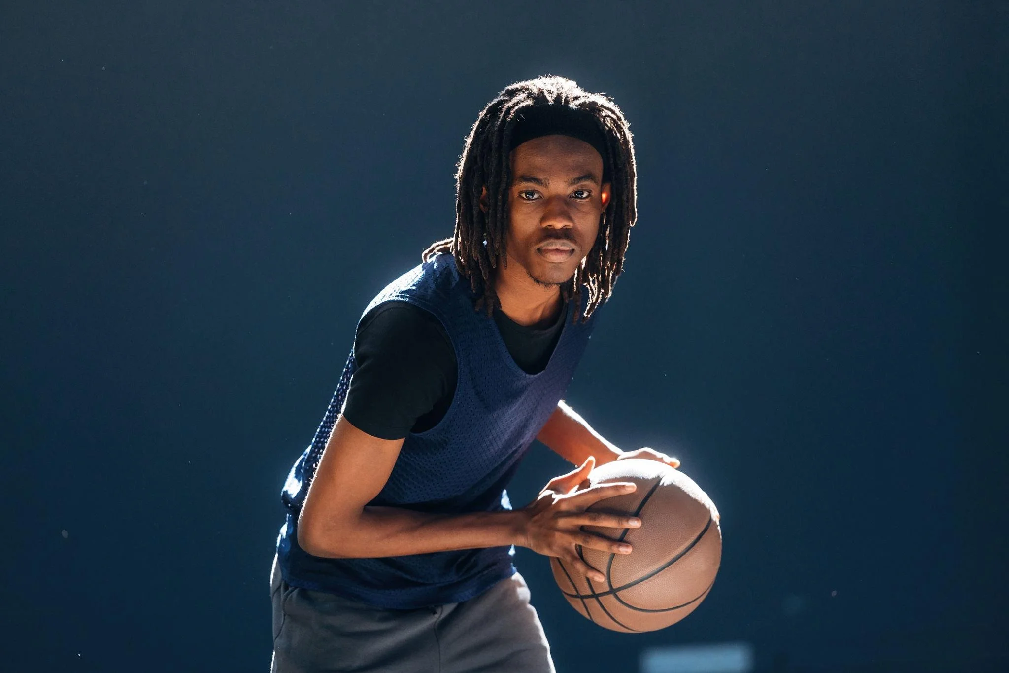 A young man with dreadlocks holding a basketball on a basketball court during daytime.