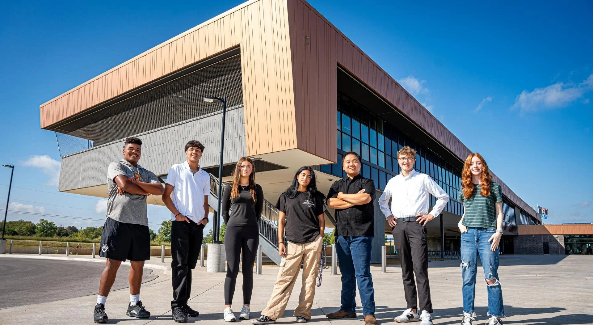 Group of diverse young students standing outside a modern school building on a sunny day.