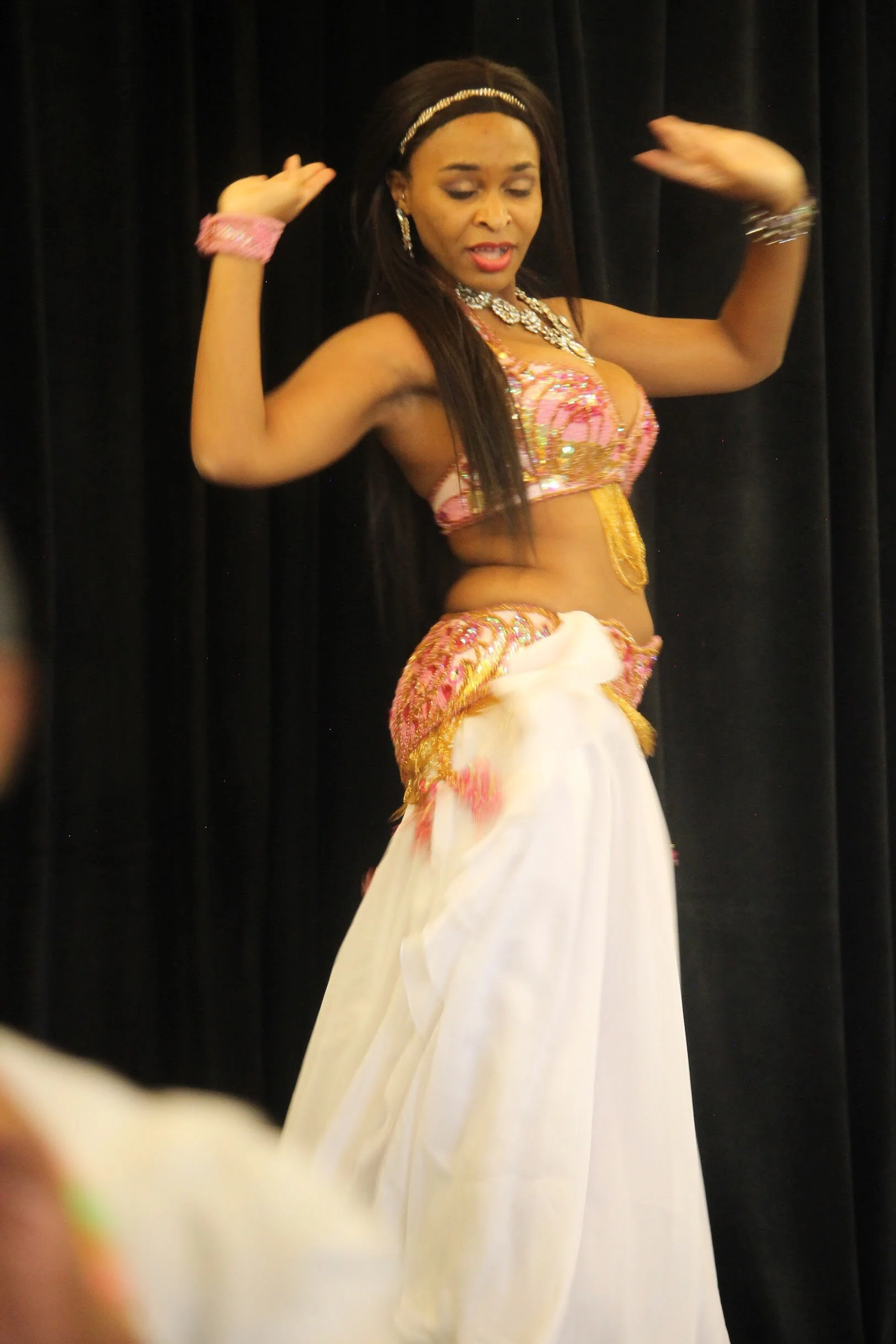 A woman dressed in traditional and ornate belly dancing costume performing on stage with a black curtain backdrop.