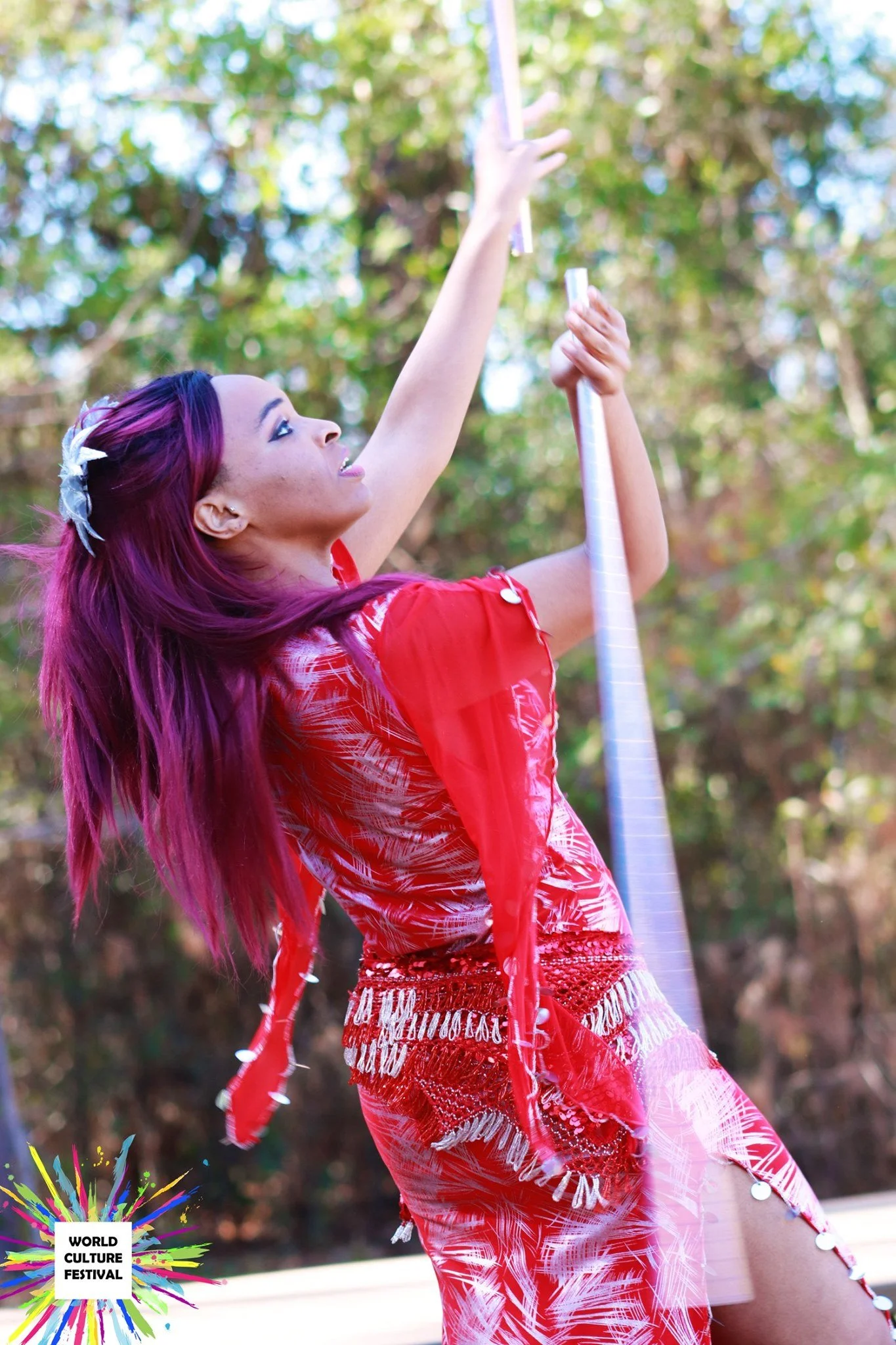 A woman with long, vibrant purple hair in traditional attire performing a dance at a cultural festival outdoors.