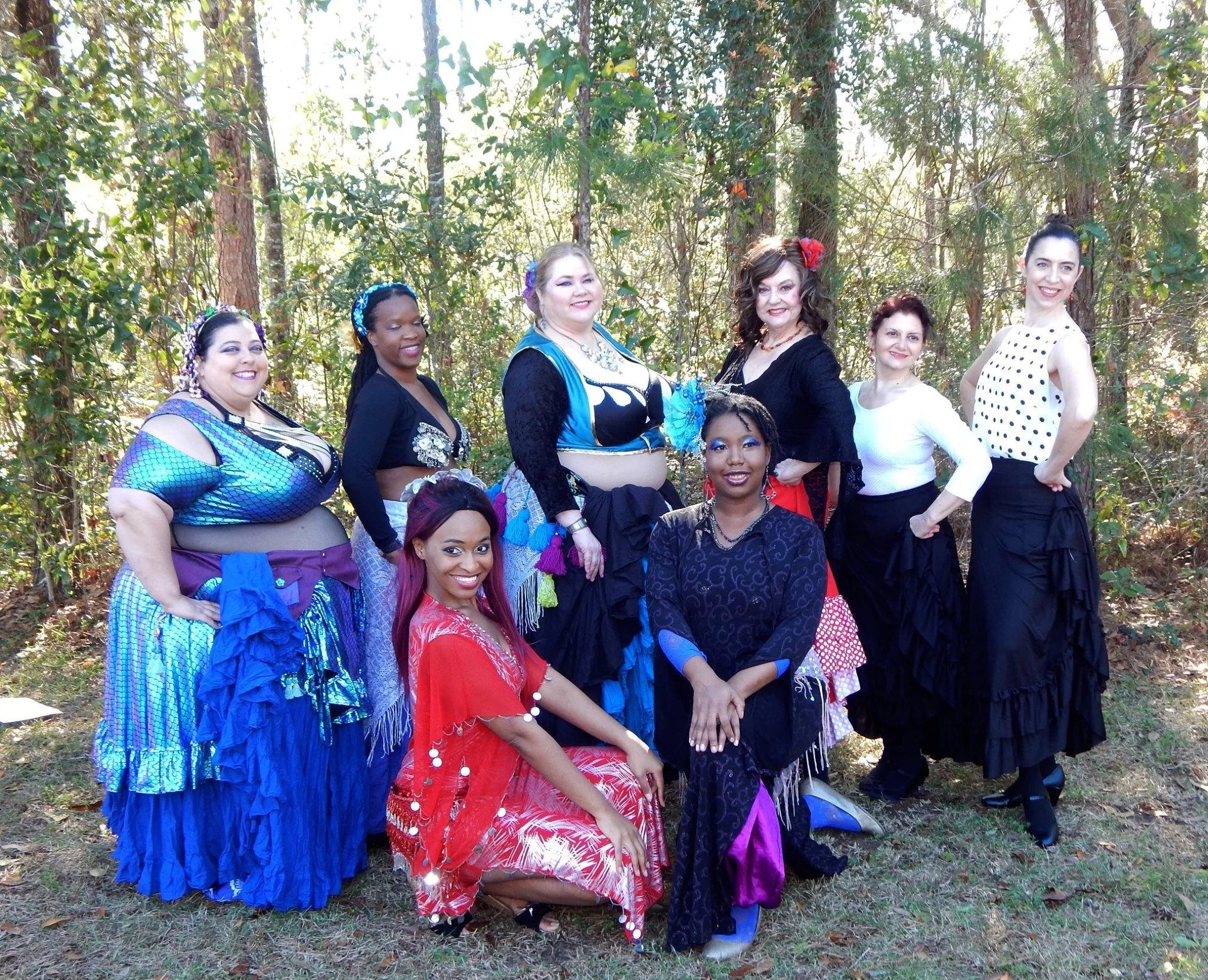 A group of women posing outdoors in a forest, wearing colorful dresses and accessories.