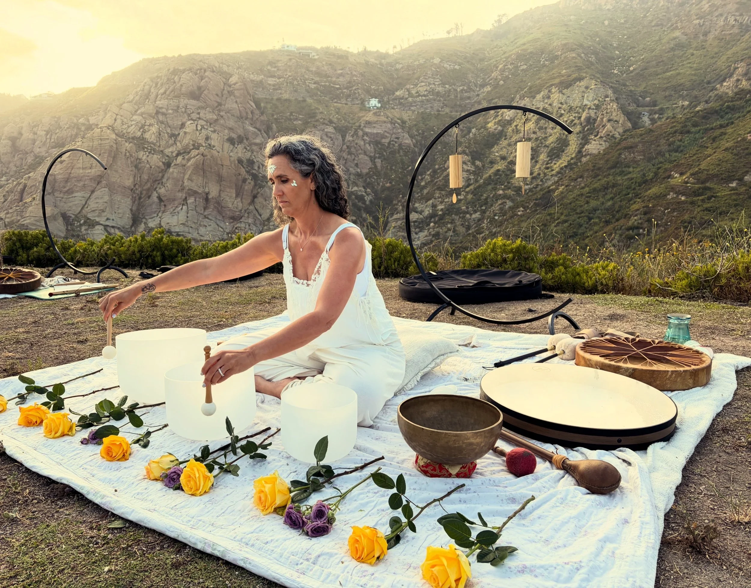 Alana leading an outdoor sound bath with crystal singing bowls, gong and flowers in the hills