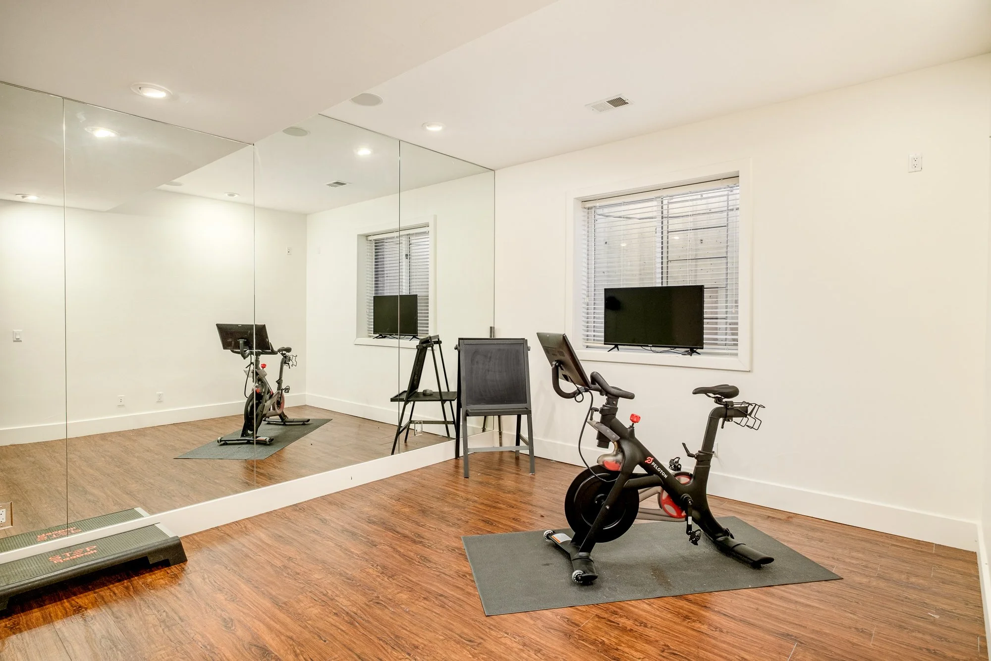 Home gym with Peloton bikes, treadmill, exercise equipment, wall mirrors, and television