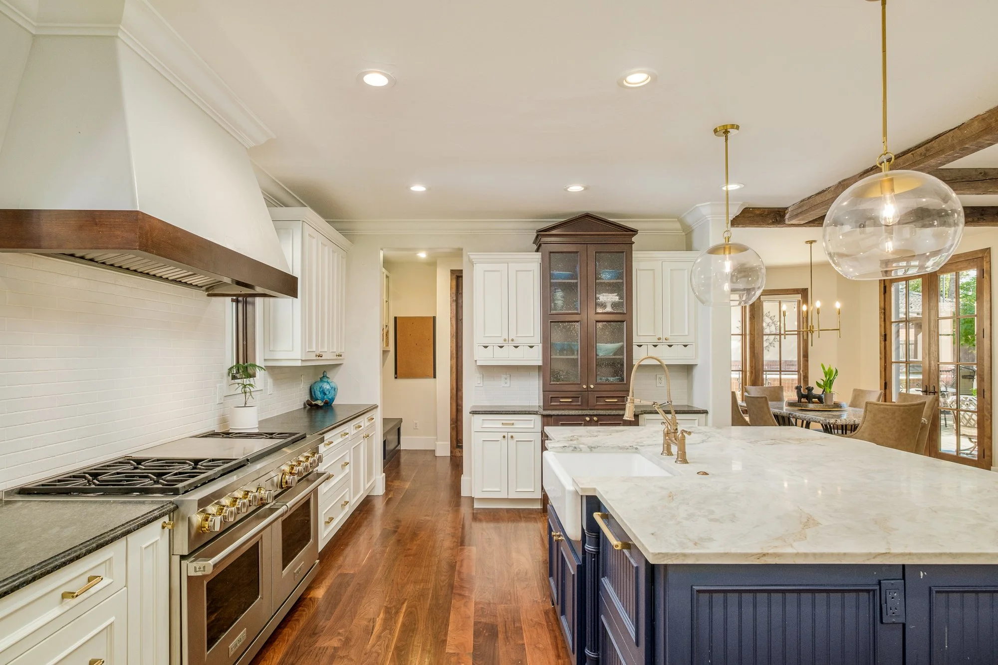 Spacious luxury kitchen with marble island, stainless steel range, white cabinetry, dark wood accents, glass pendant lights, and adjoining dining area.