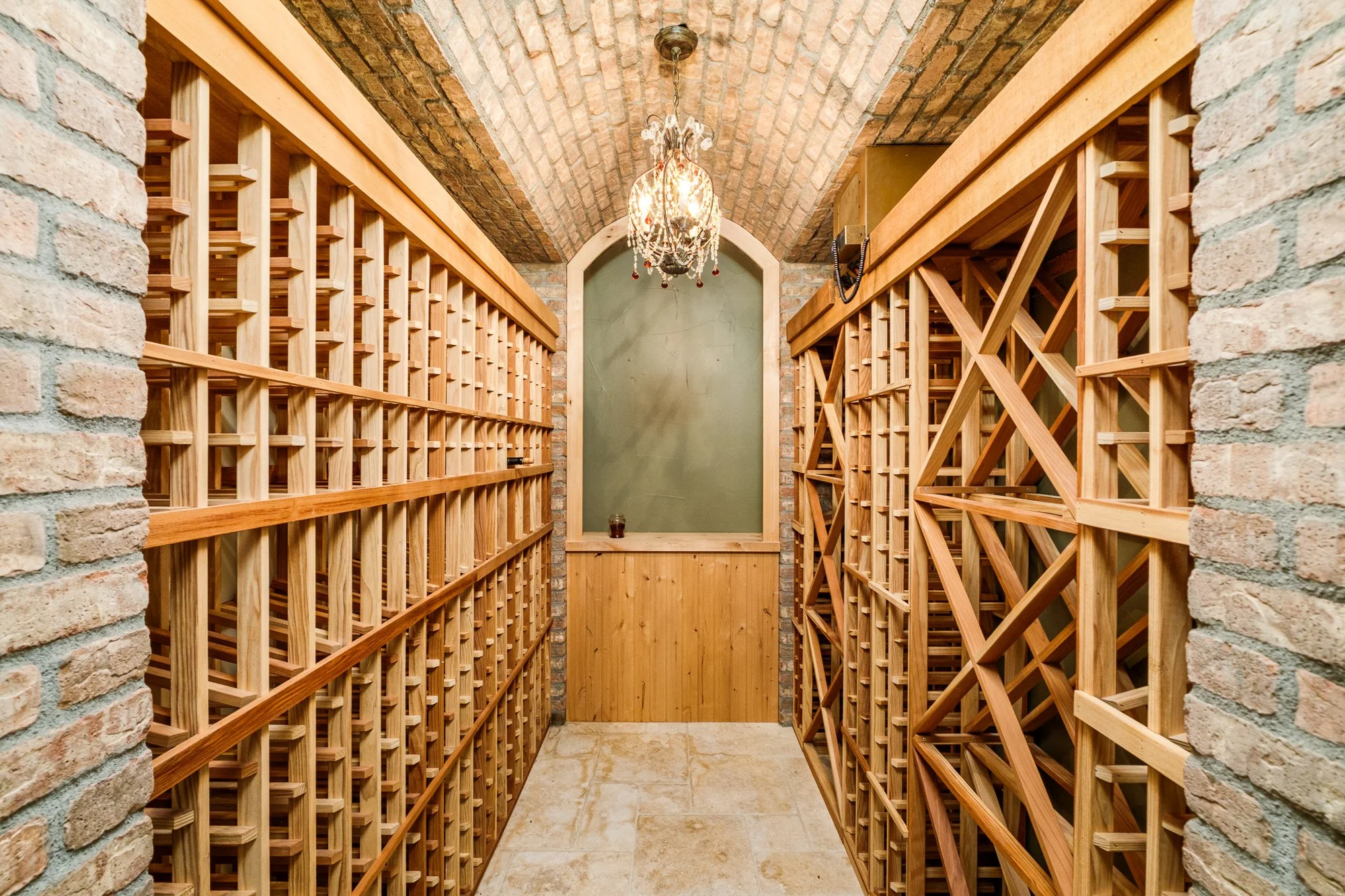 Luxury wine cellar with wooden wine racks, exposed brick walls, arched ceiling, and chandelier