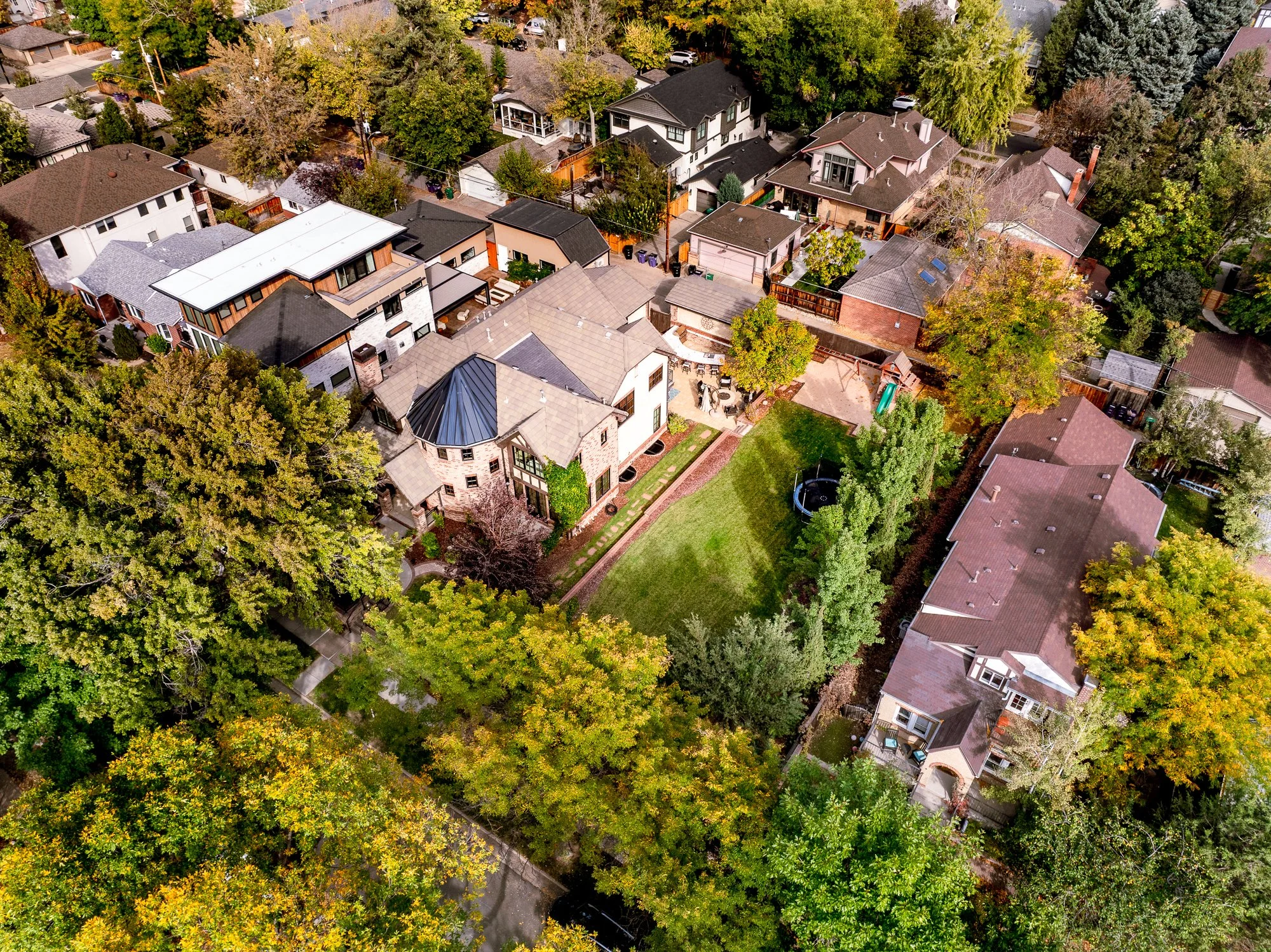 Aerial view of a leafy residential neighborhood with detached homes, backyards, mature trees, and a spacious green lawn.