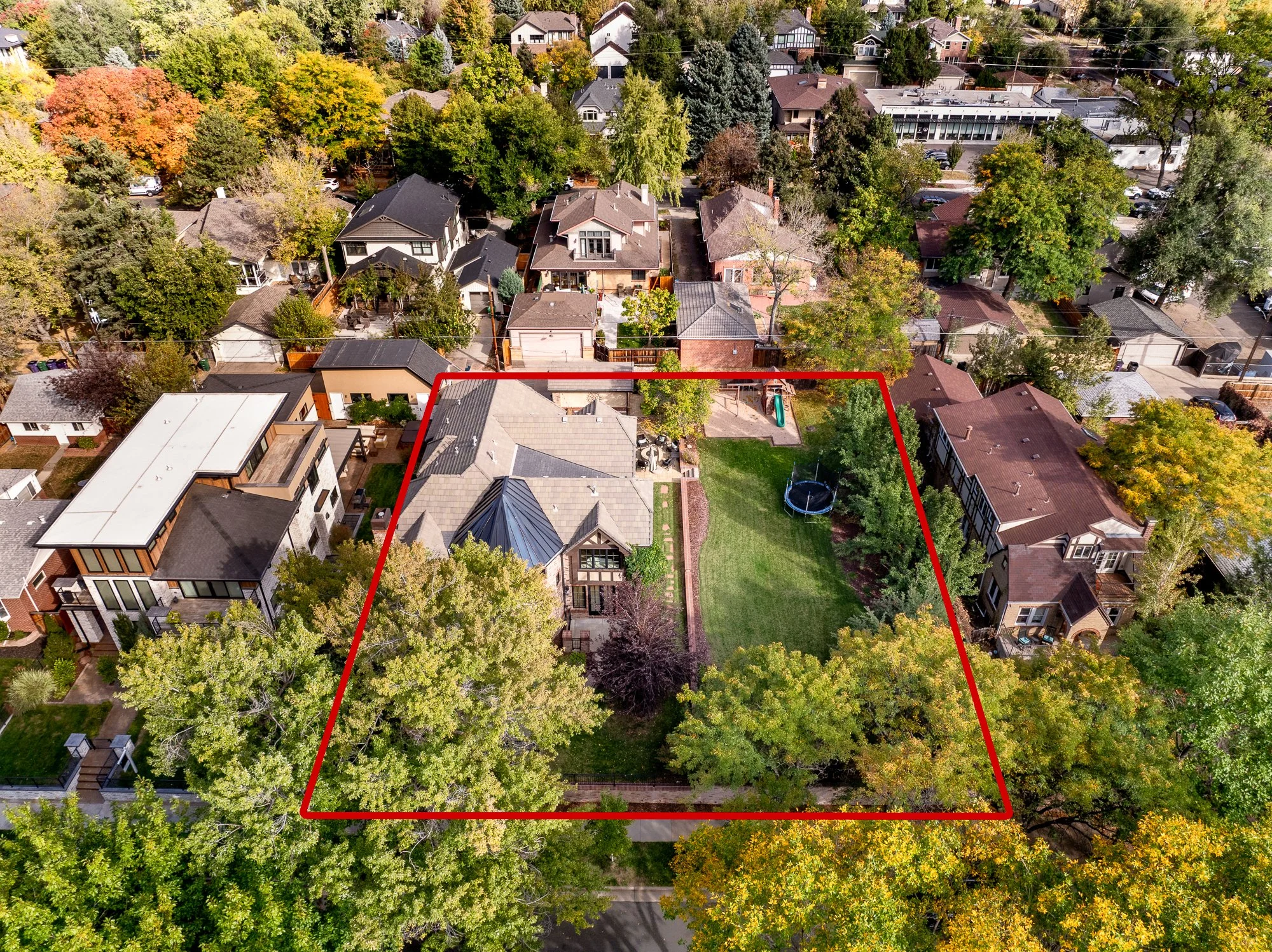 Aerial view of a tree-lined residential neighborhood with a large property outlined in red, showing a home, expansive lawn, and backyard trampoline.