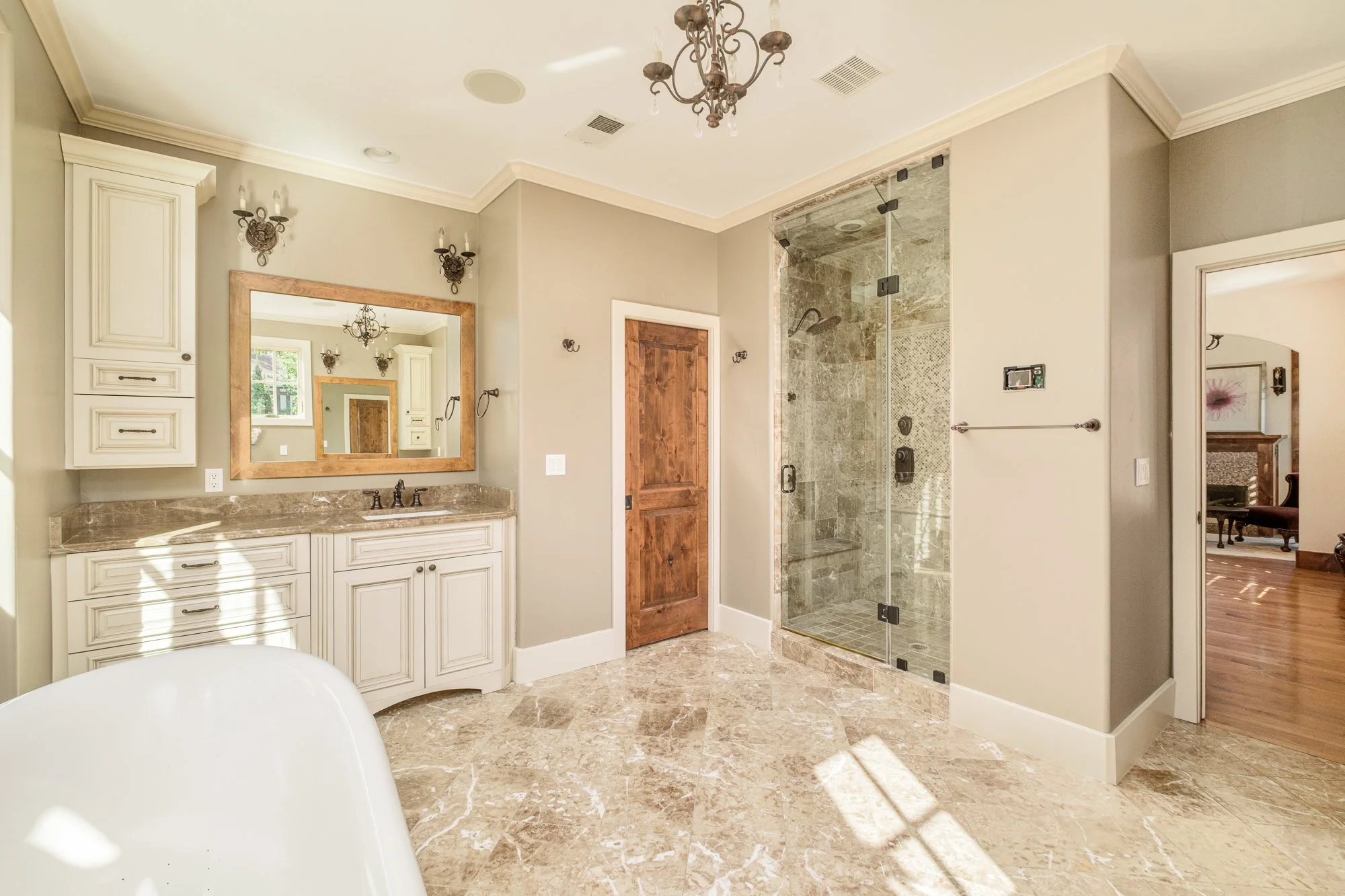 Spacious luxury bathroom with marble floors, double vanity, ornate mirror, freestanding bathtub, and glass-enclosed walk-in shower