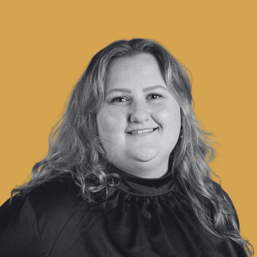 Black and white portrait of a woman with wavy hair, smiling, against a mustard yellow background.