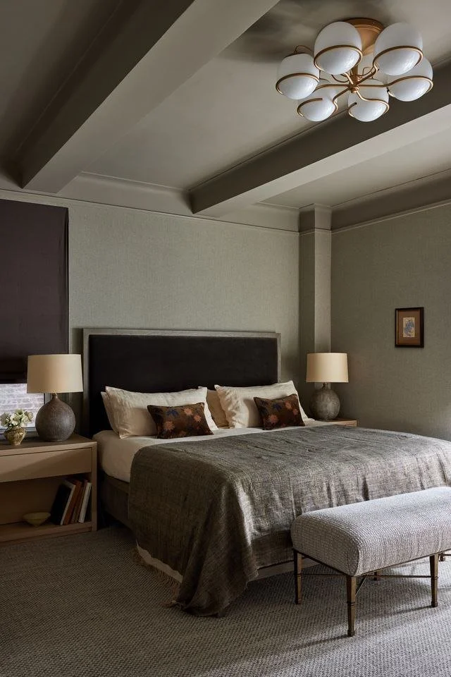 Riverside Drive bedroom with ceiling beams, a sculptural chandelier, upholstered bed and layered neutral textiles.