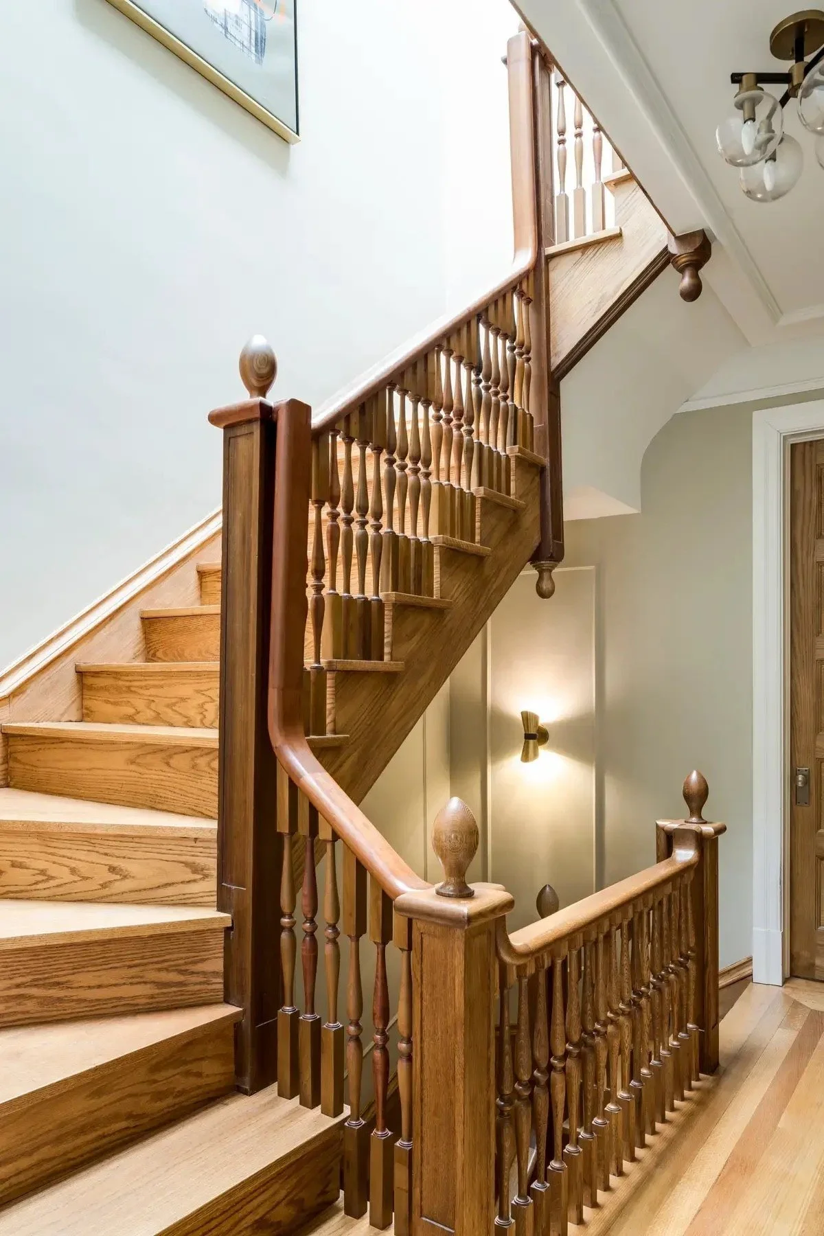 West 138th Street brownstone staircase with warm wood balustrades, period architectural details and a tall arched window.
