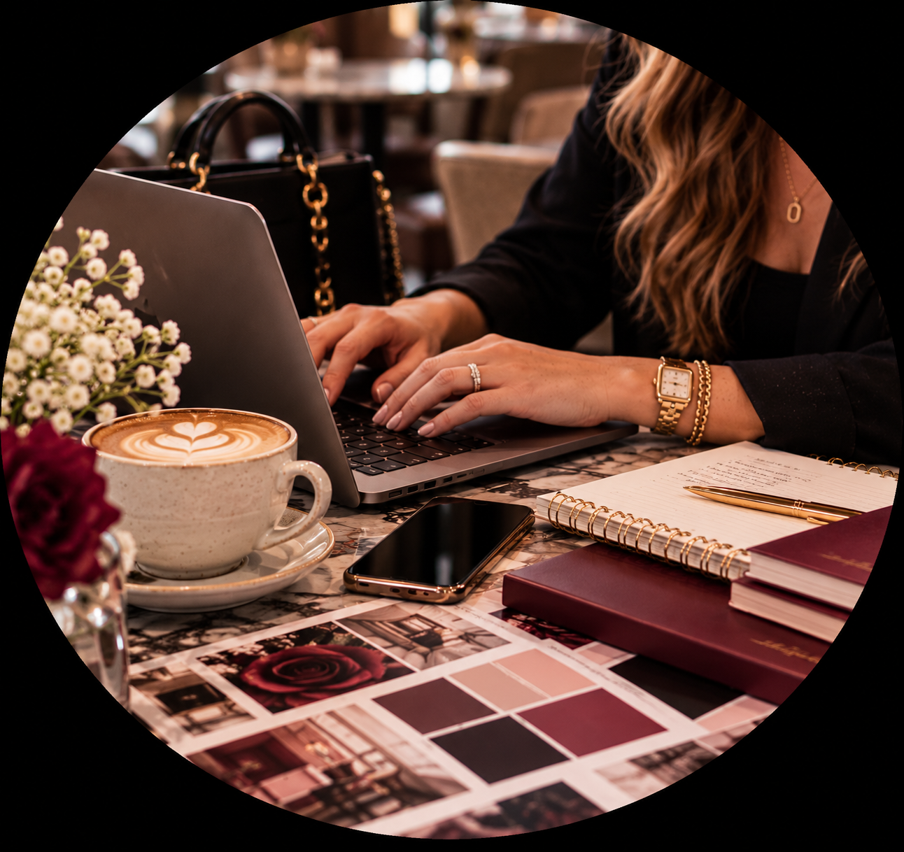 Woman working on a laptop at a cafe with coffee, smartphone, notebook, and flowers on the table