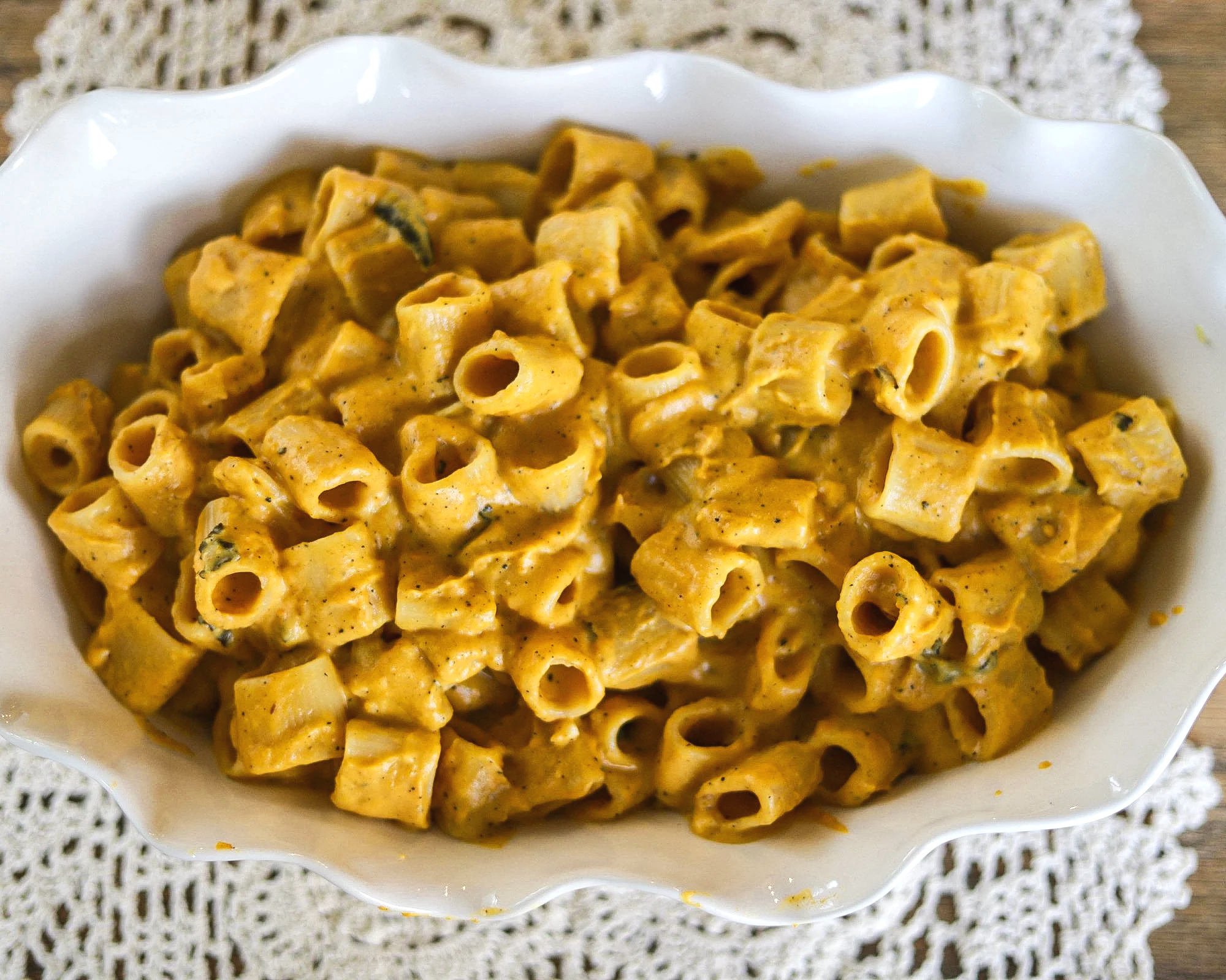 Creamy orange sauce-coated tube pasta served in a white scalloped dish