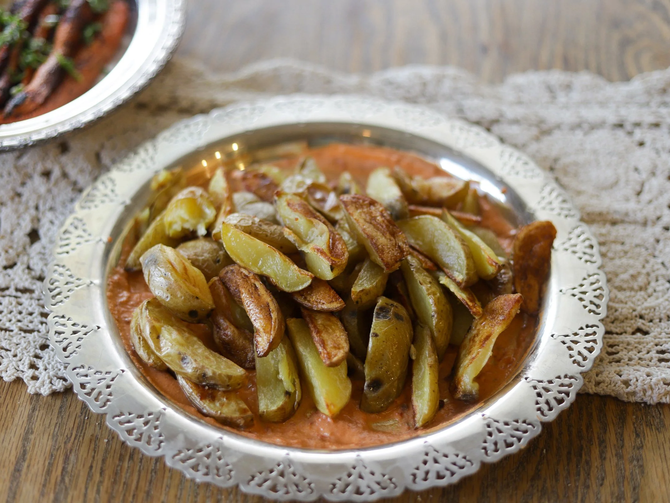 Roasted potato wedges served over tomato sauce on an ornate silver platter
