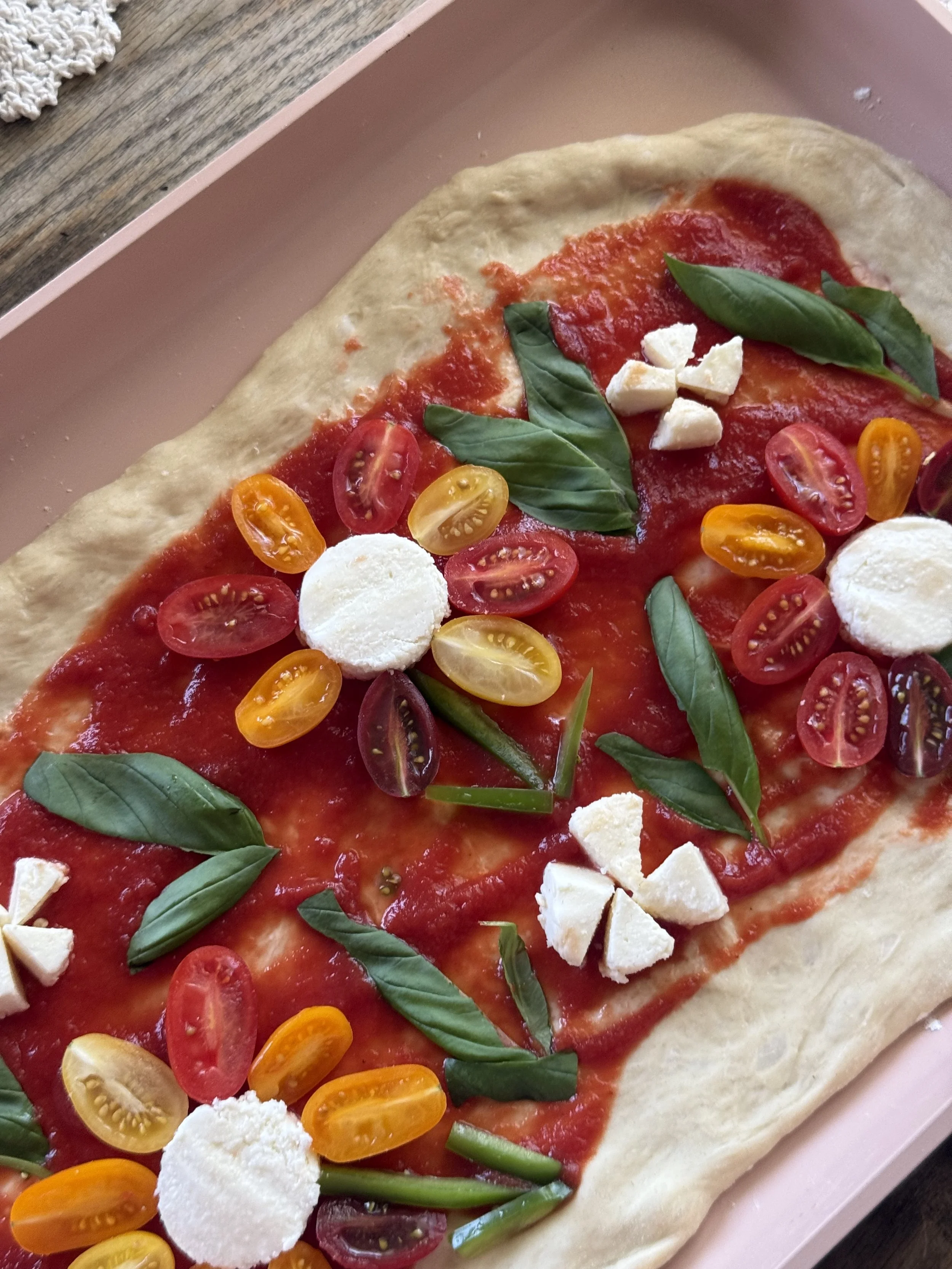Close-up of homemade pizza topped with tomato sauce, sliced cherry tomatoes, fresh basil, and mozzarella cheese.