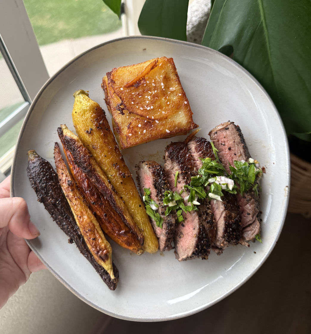 Plate of sliced medium-rare steak with chimichurri, roasted carrots, and a golden baked potato gratin.