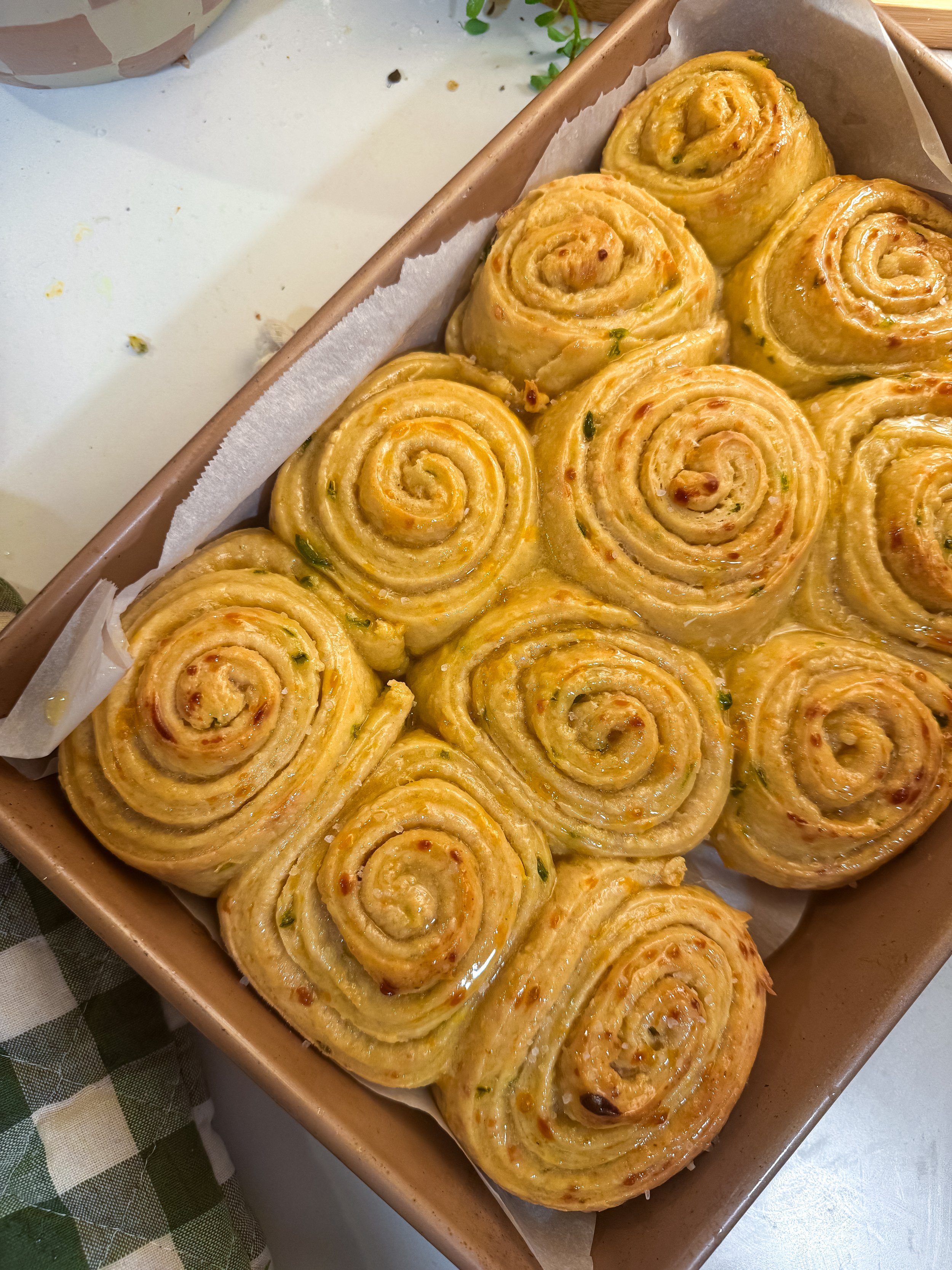 Golden-brown spiral savory pastries with herbs arranged on parchment in a baking tray