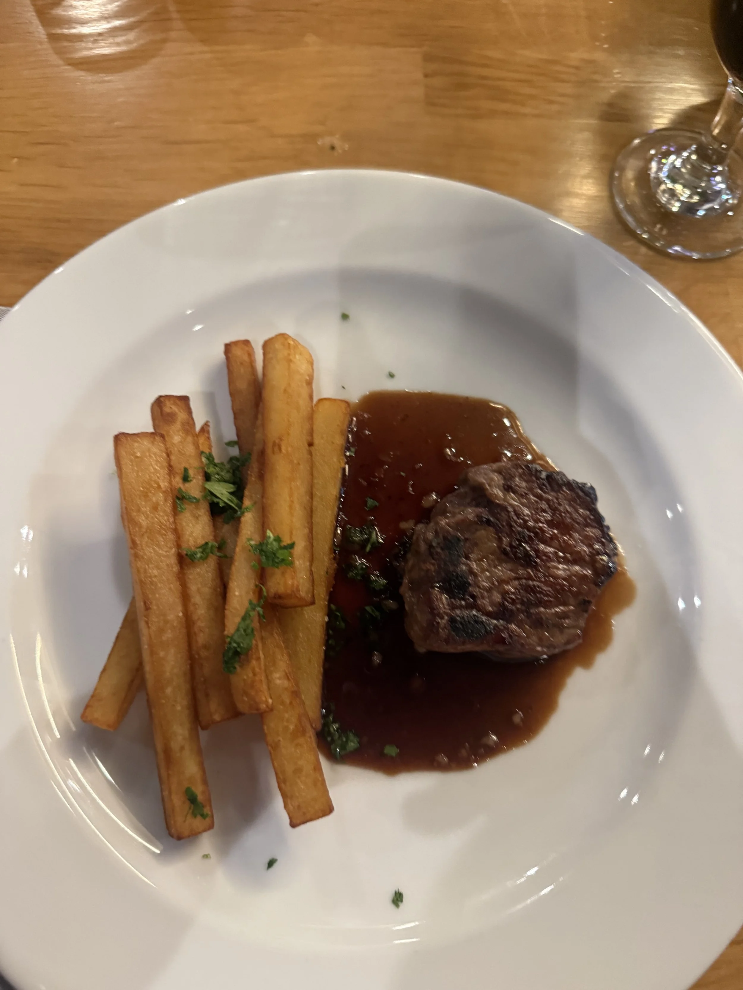 Grilled steak with crispy fries, brown sauce, and chopped parsley on a white plate.