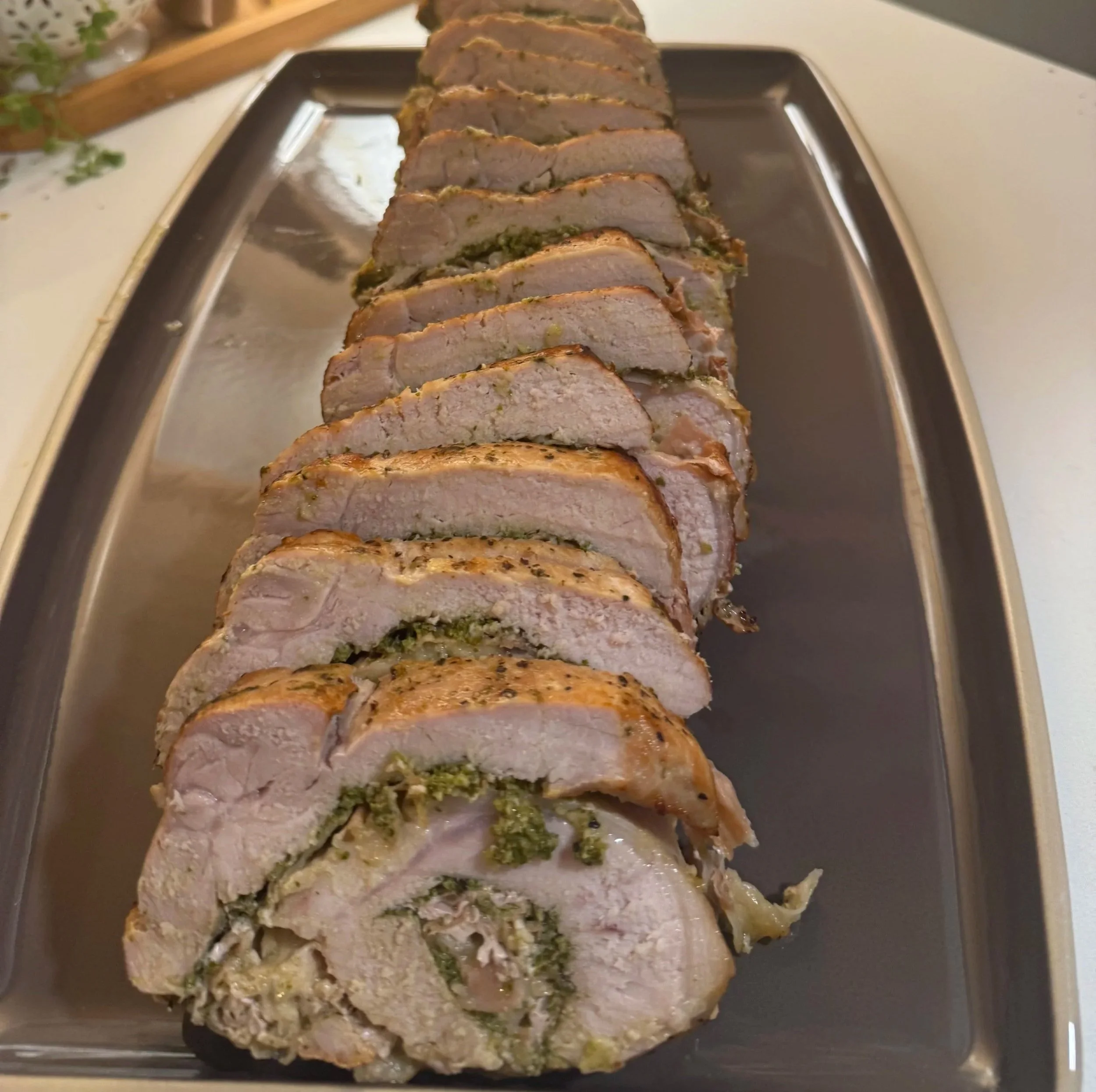 Sliced herb-stuffed pork roast arranged on a rectangular serving platter