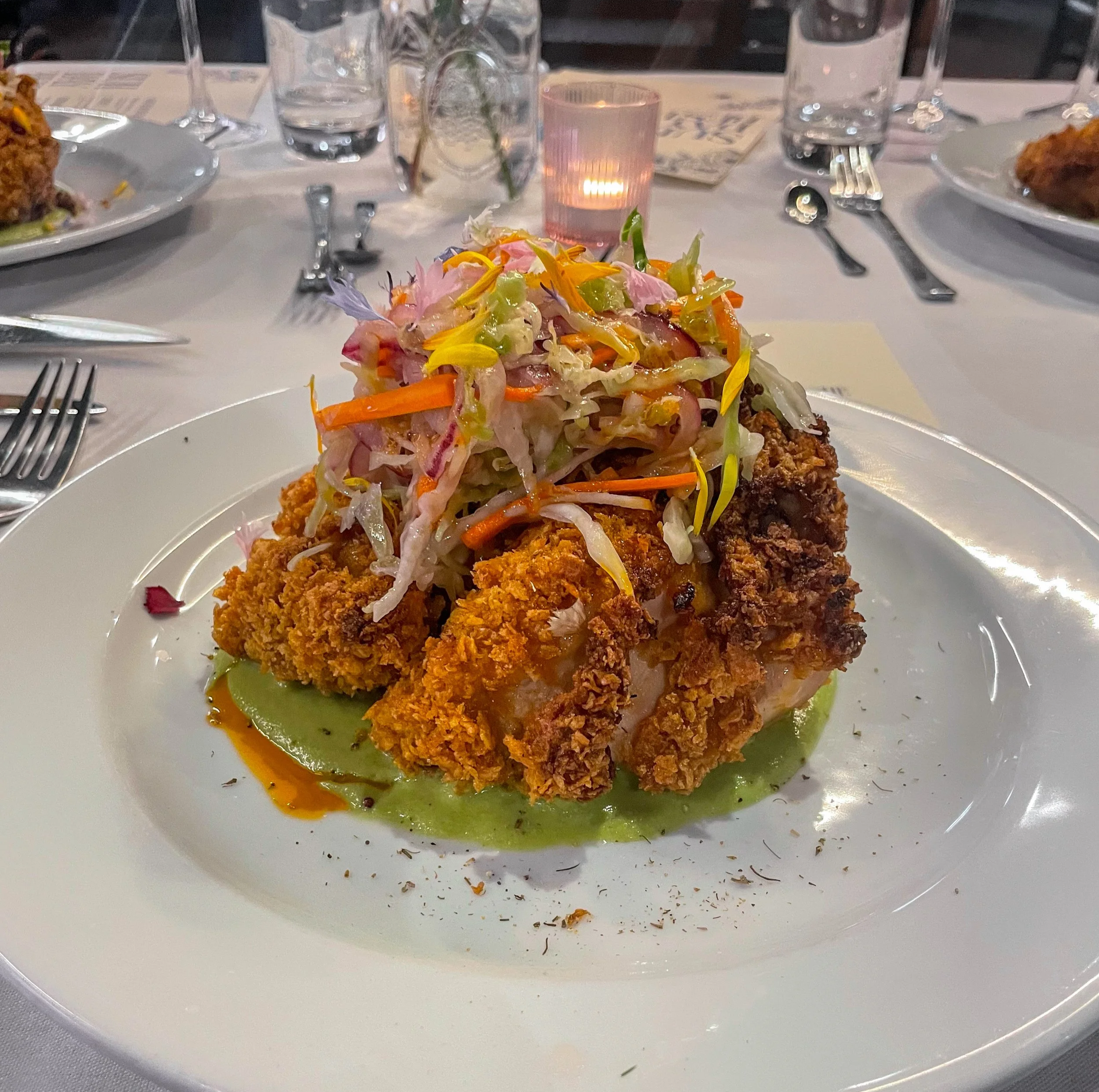 Gourmet plate of crispy fried seafood topped with shaved vegetables and edible flowers over green sauce