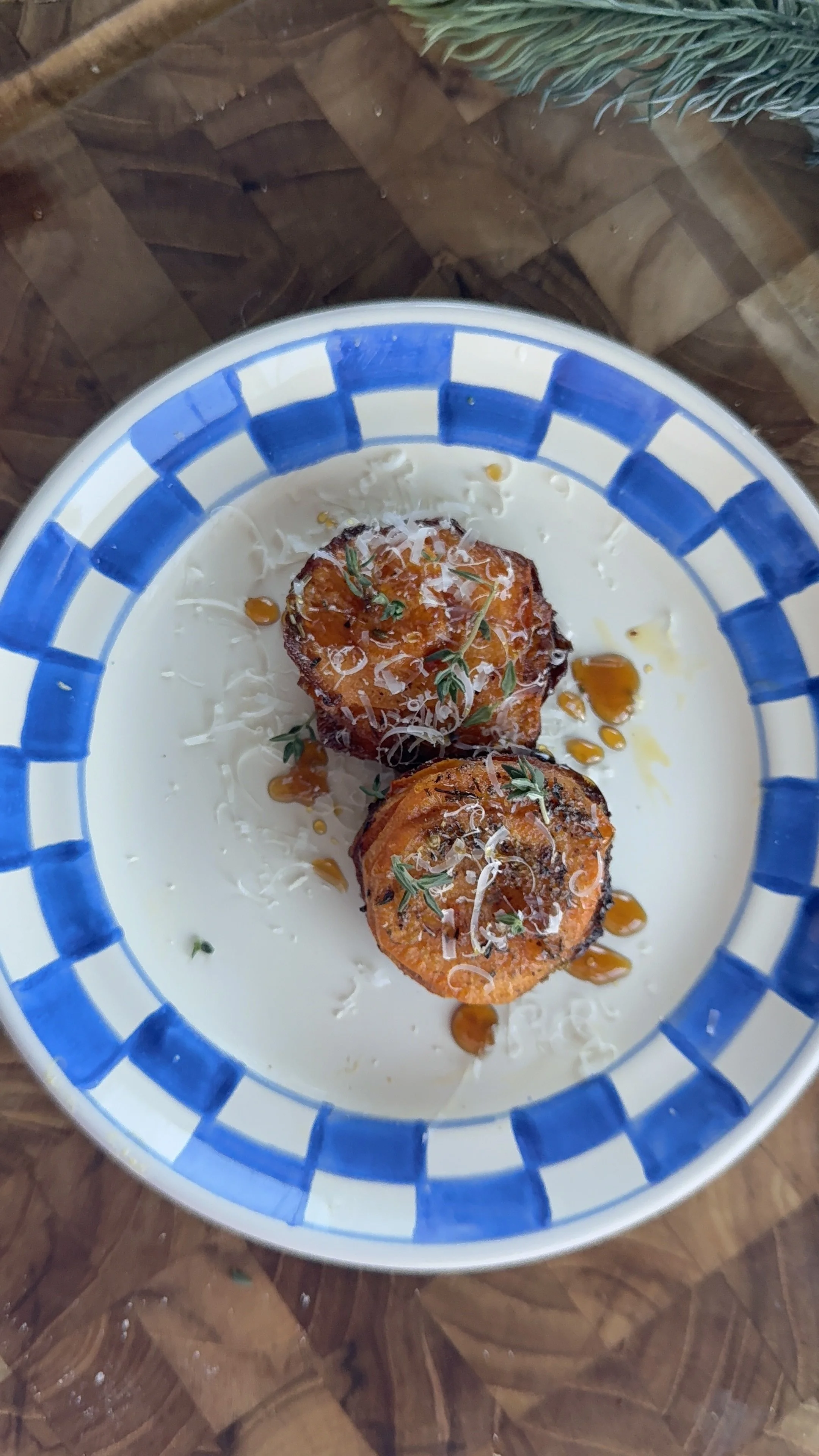 Roasted sweet potato wedges topped with shredded cheese, herbs, and honey on a blue-and-white plate.
