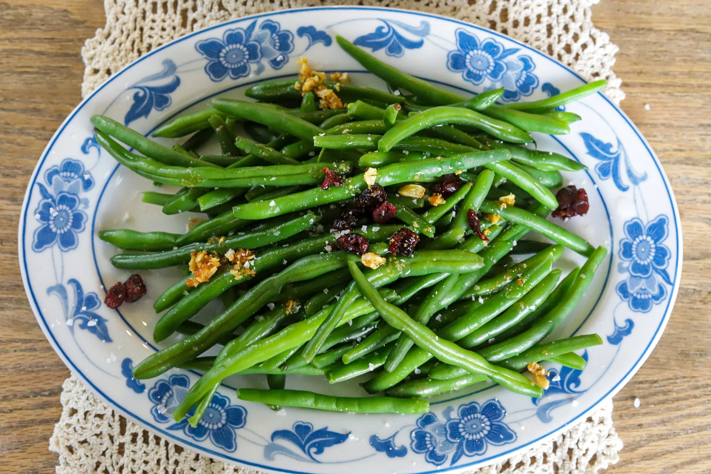 Seasoned green beans with dried cranberries and crispy garlic on a blue-and-white serving platter