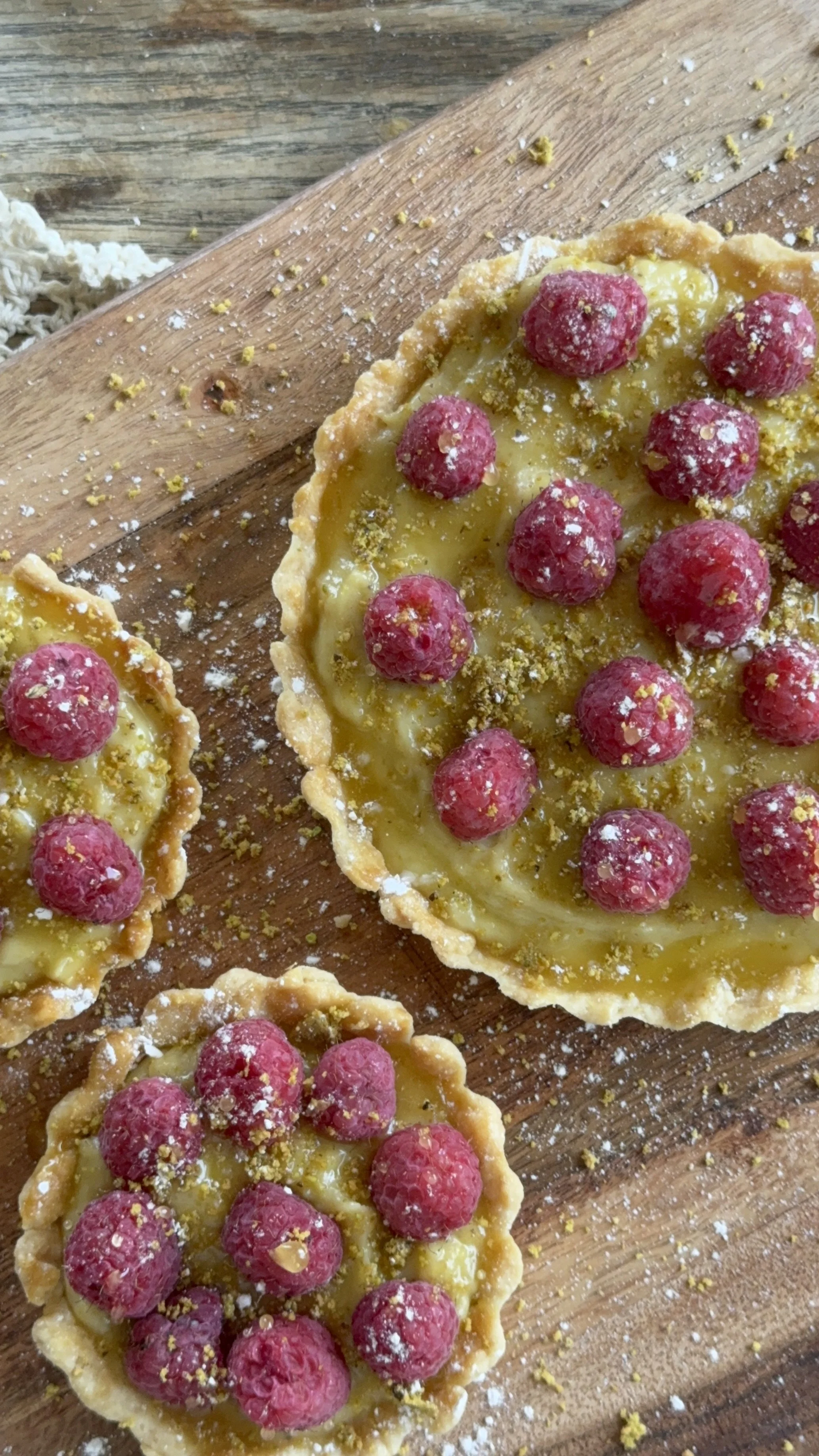 Raspberry and pistachio tartlets dusted with powdered sugar on a wooden board