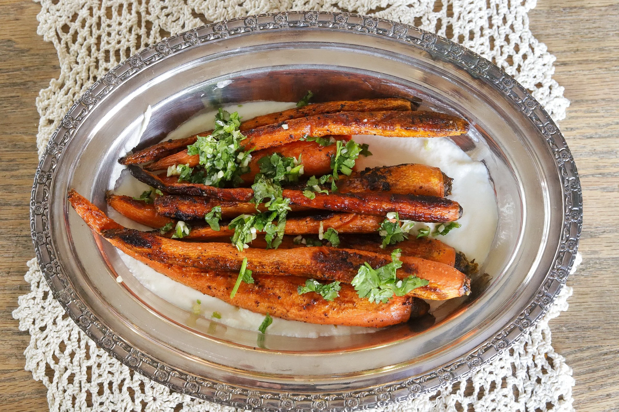 Roasted carrots with chopped fresh herbs served over creamy sauce on an ornate platter